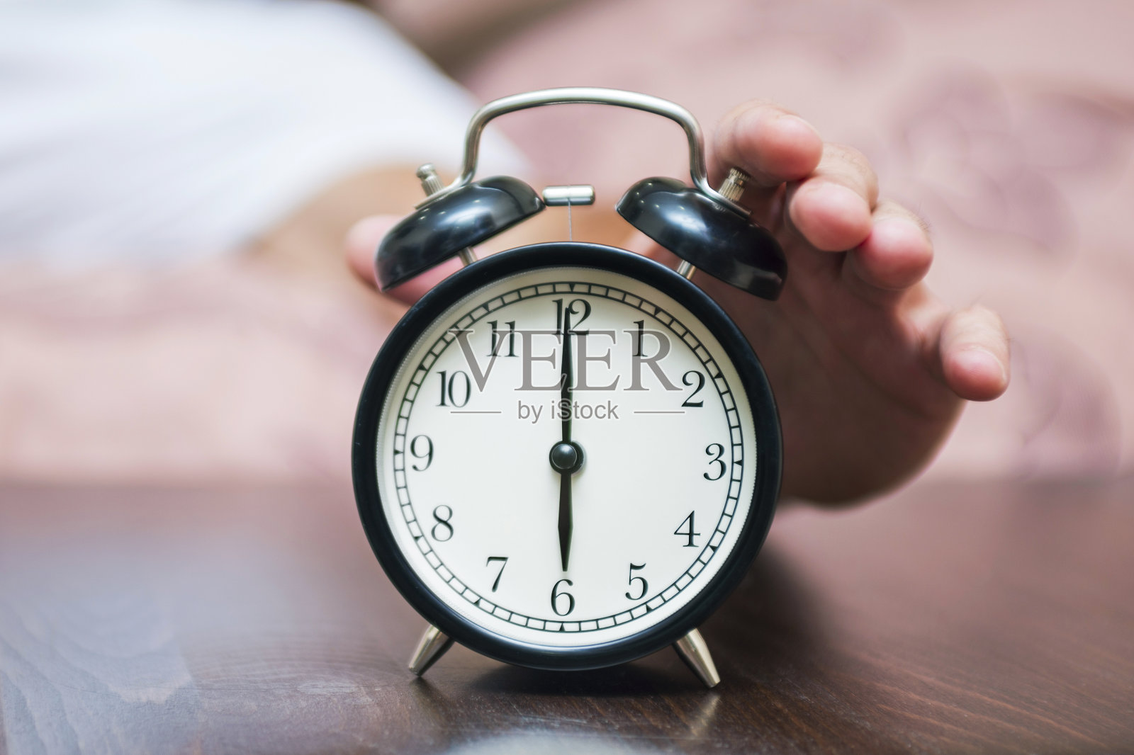 一个正在睡觉的年轻人被卧室里的闹钟吵醒了。早上，一个男人躺在床上关掉闹钟照片摄影图片