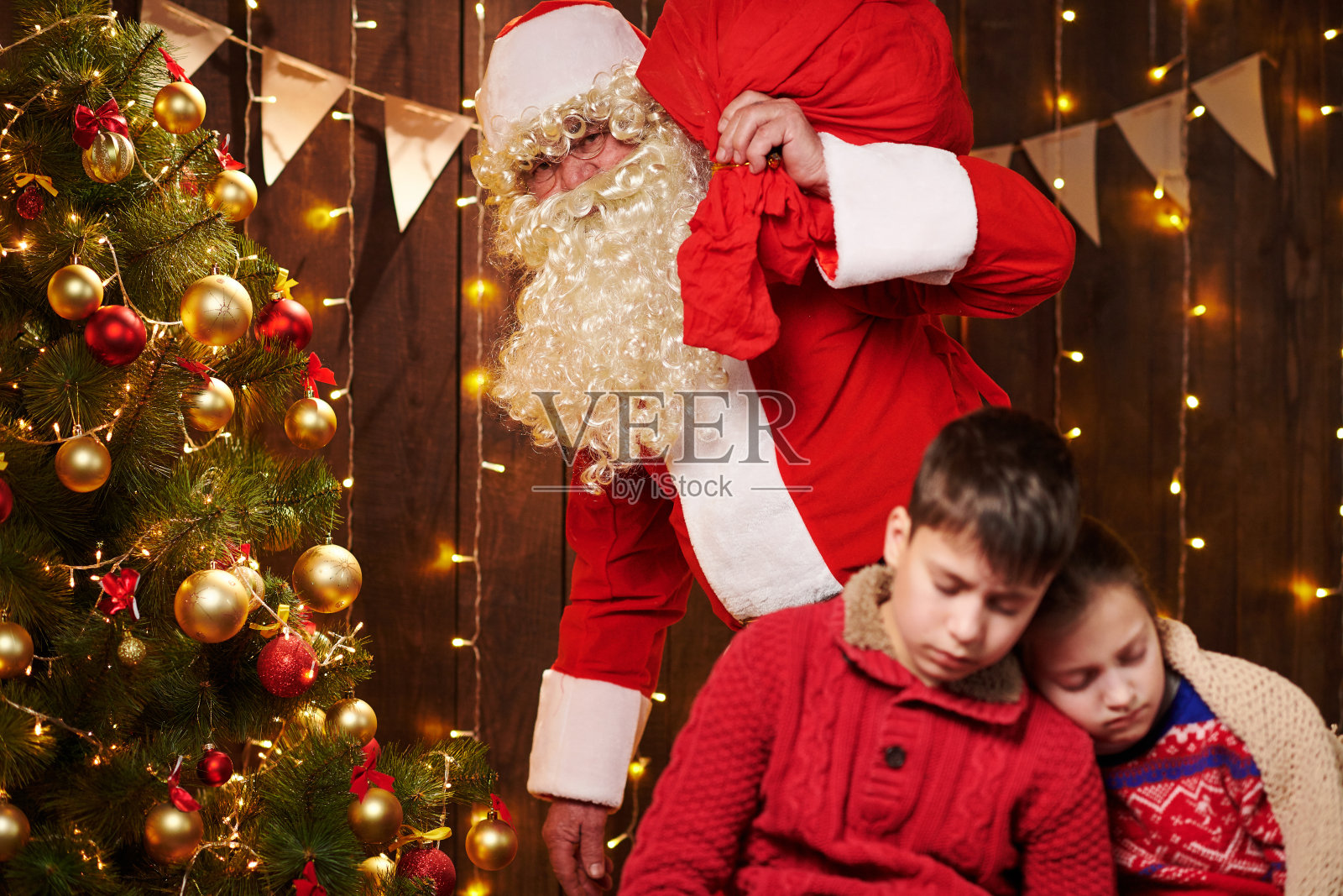 孩子们等圣诞老人等了很长时间，现在他们睡着了，圣诞老人静静地走到圣诞树上给礼物——圣诞快乐，节日快乐!照片摄影图片