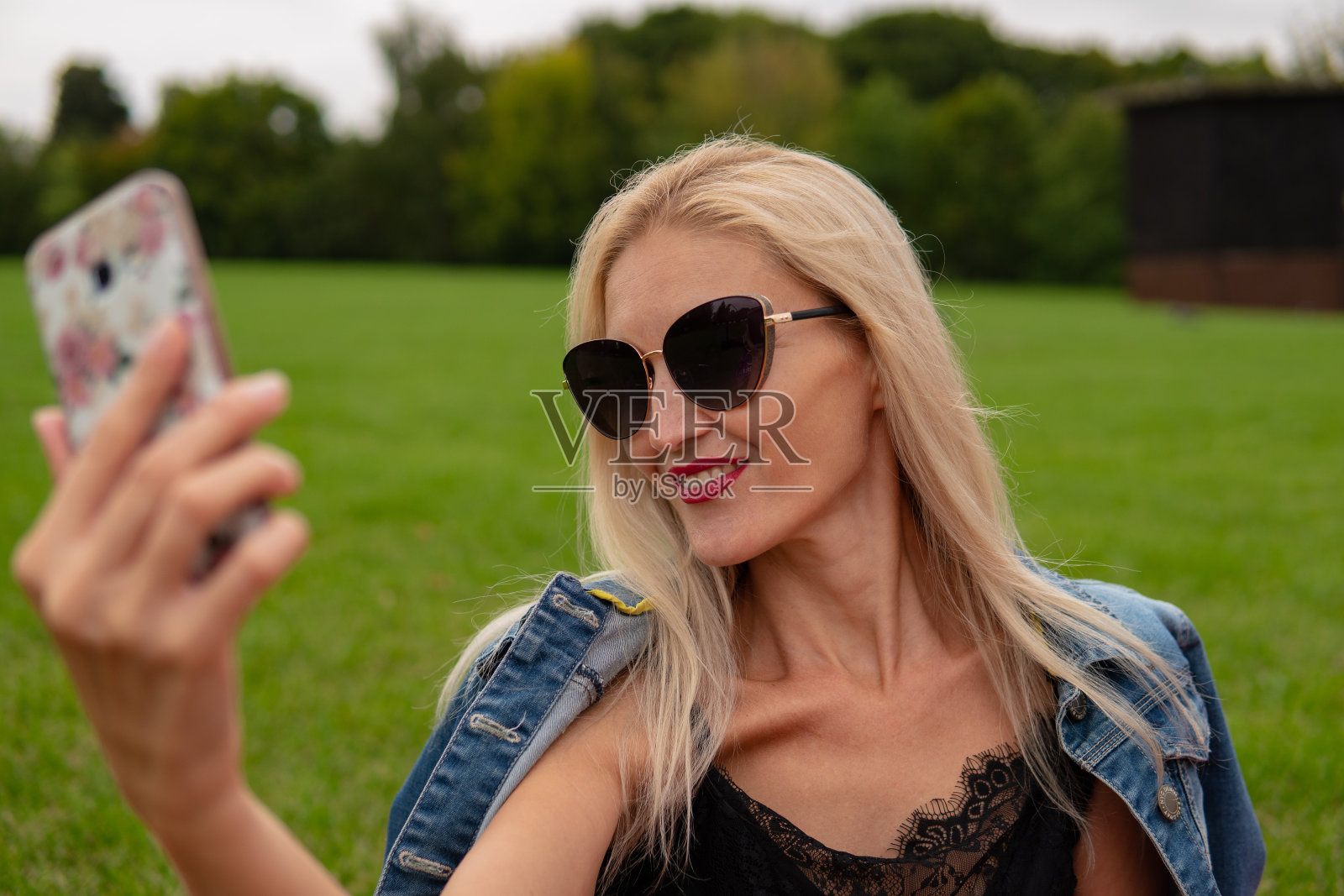 一个女孩戴着光致变色眼镜在一片美丽的森林后面的田野上自拍。照片摄影图片