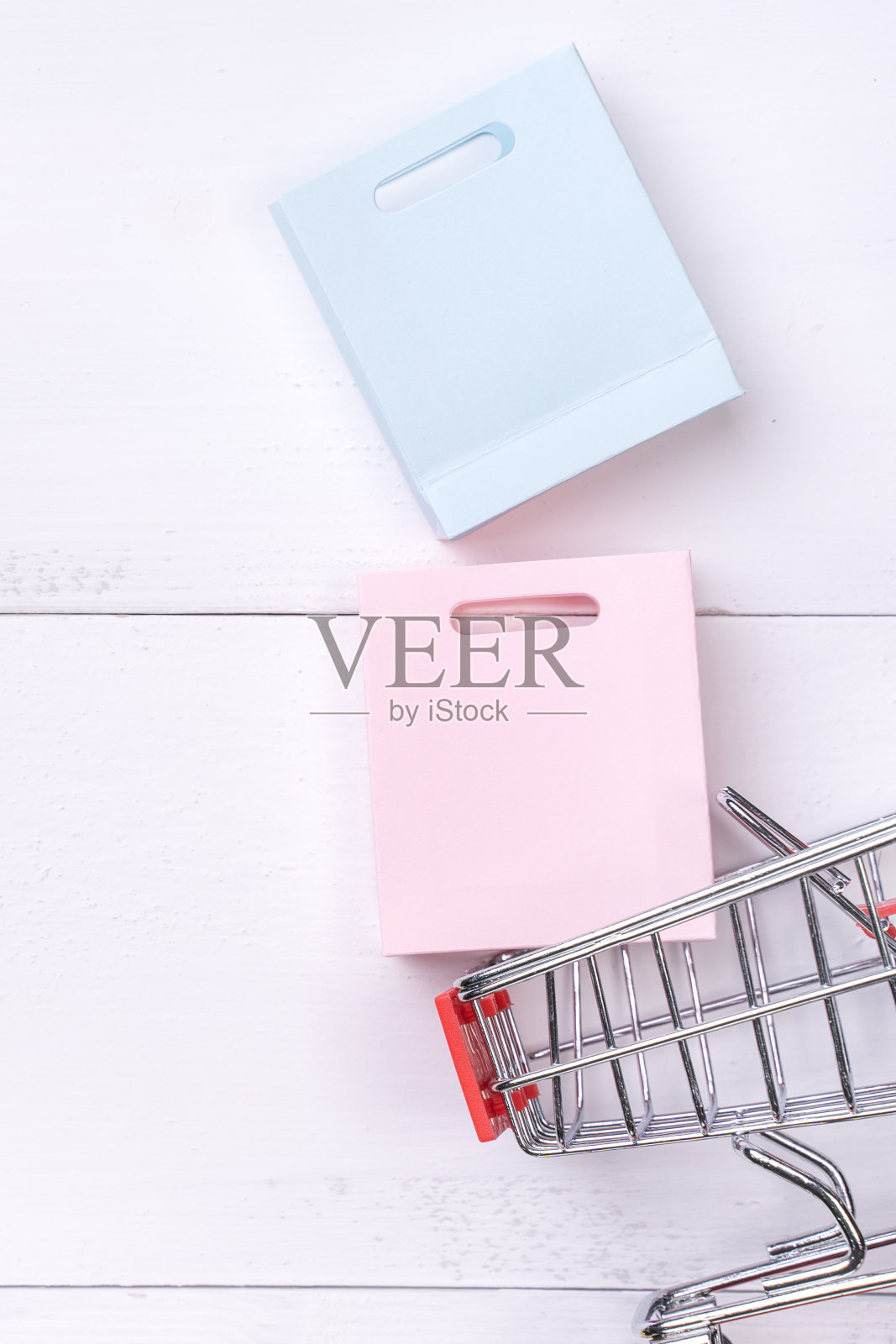 抽象的设计元素，年度销售，购物季节的概念，小手推车与彩色纸袋在白色木制桌子的背景。照片摄影图片