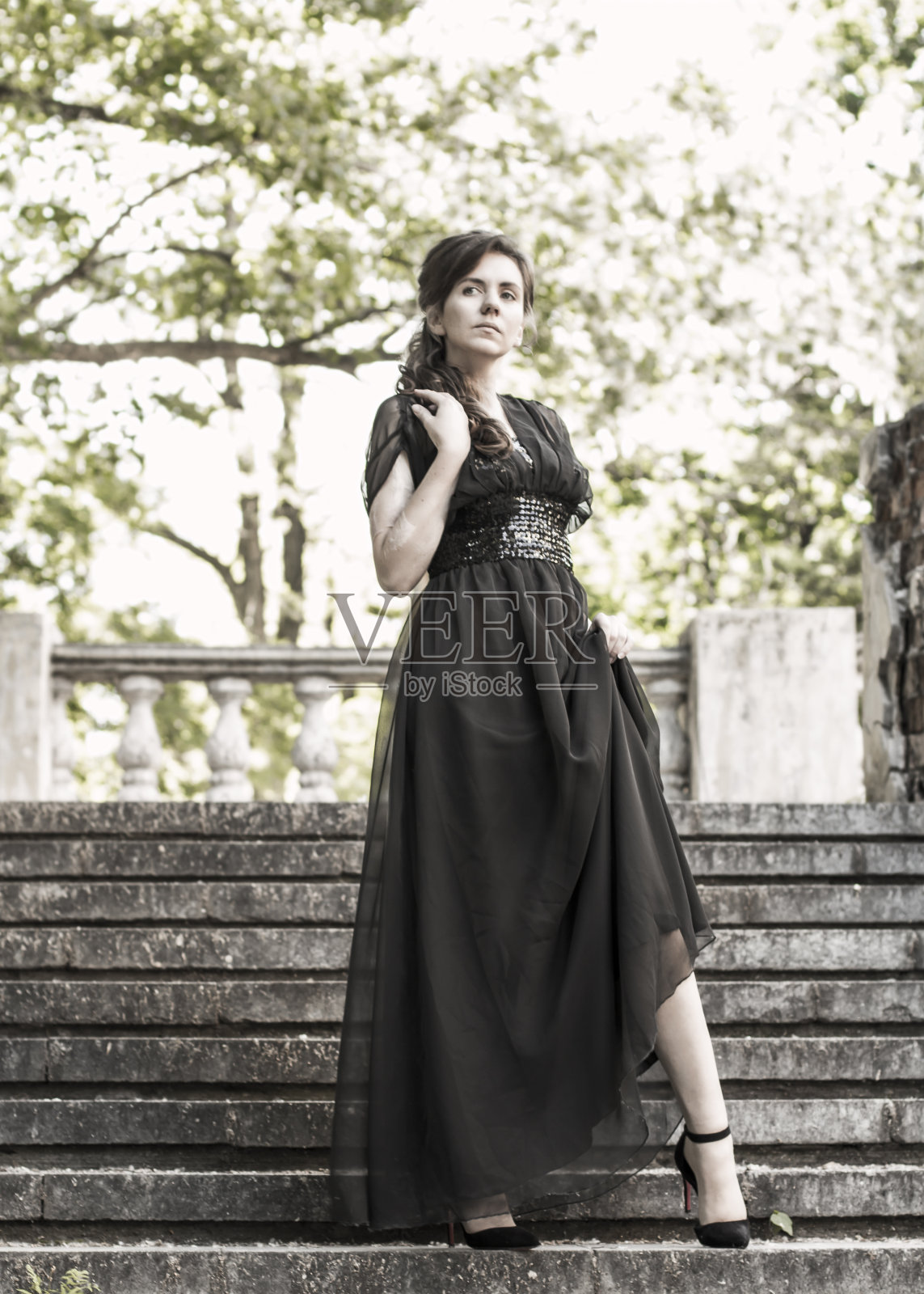 穿着黑色晚礼服的漂亮女孩站在一座废弃宫殿的台阶上。有伤疤的漂亮女人。年轻女孩的复古风格。女孩走上楼梯。漂亮的女人照片摄影图片