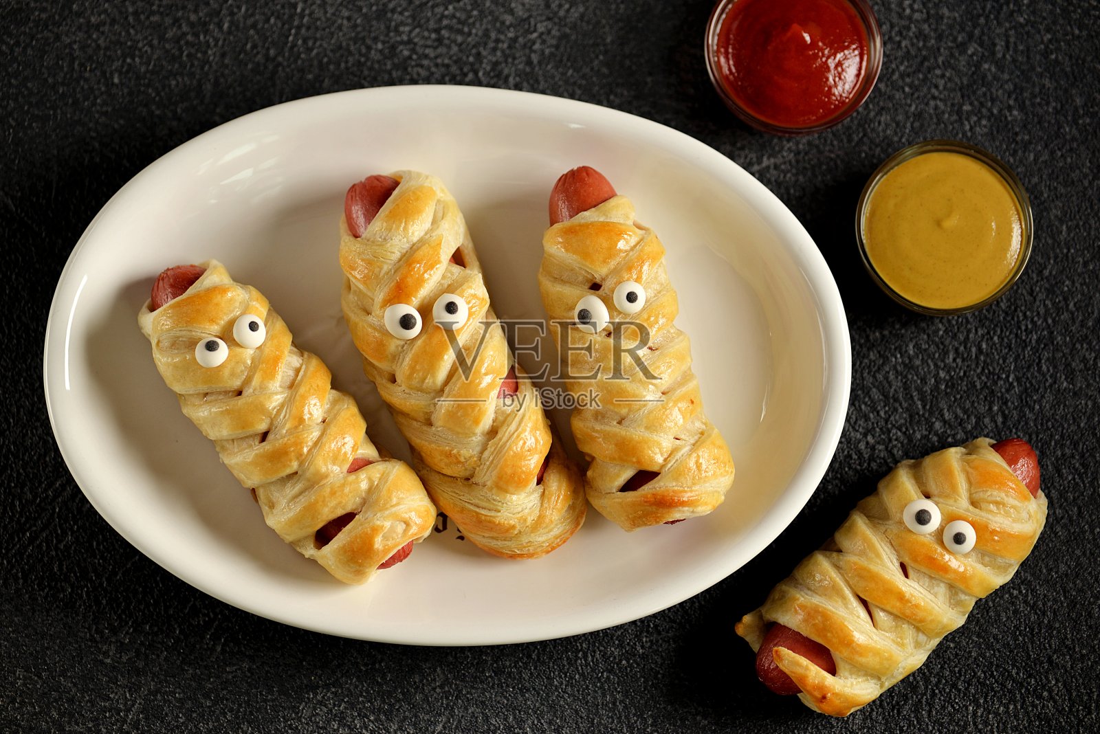 万圣节派对上的可爱香肠“妈咪”搭配番茄酱和芥末。孩子们的食物。照片摄影图片