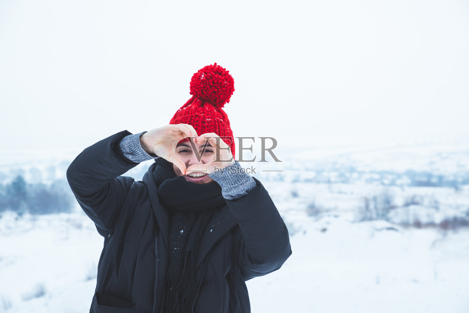 戴红帽子的女人用手做爱的象征。冬天的时间。降雪照片摄影图片