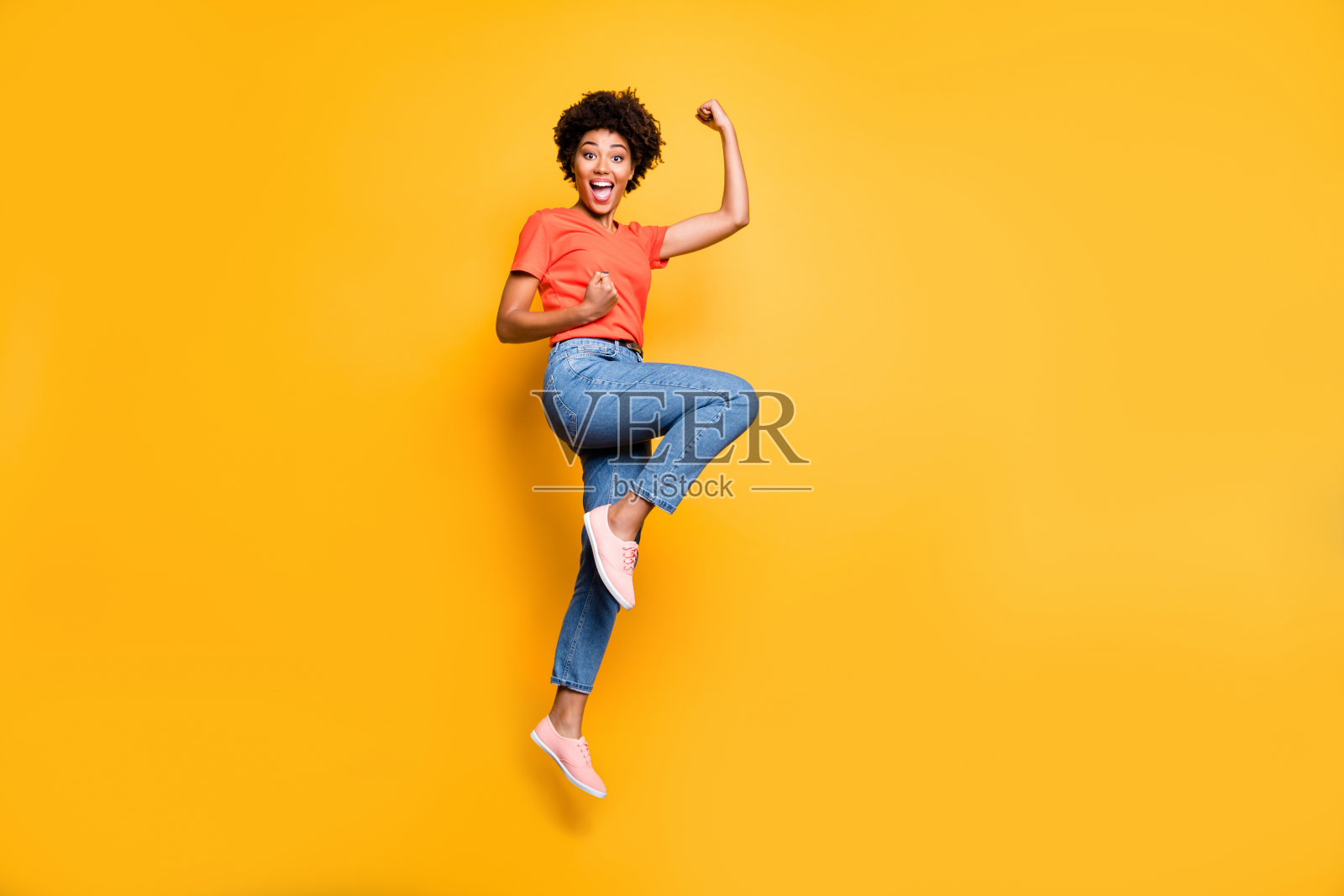 全身大小的照片，欢快可爱的黑色女友跳起来穿着牛仔裤牛仔t恤鞋欣喜孤立在黄色鲜艳的颜色背景照片摄影图片
