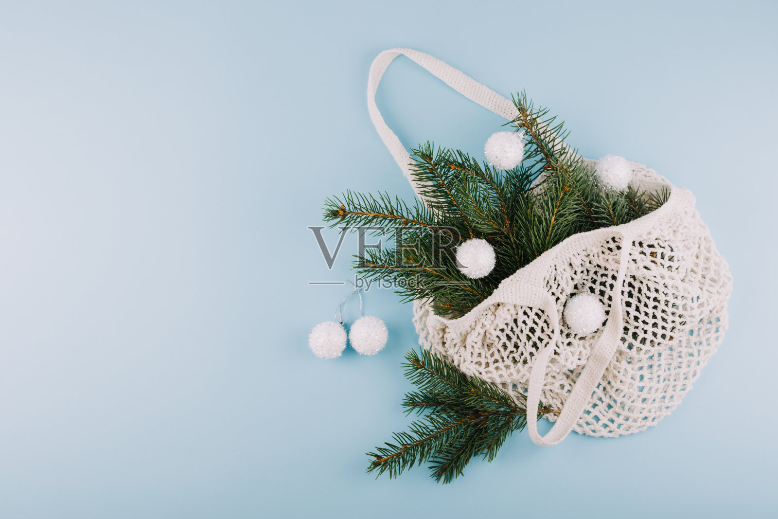 新年圣诞平铺顶视图构成。时尚现代棉网袋与冷杉树枝和蓬松的圣诞球在蓝色的背景照片摄影图片