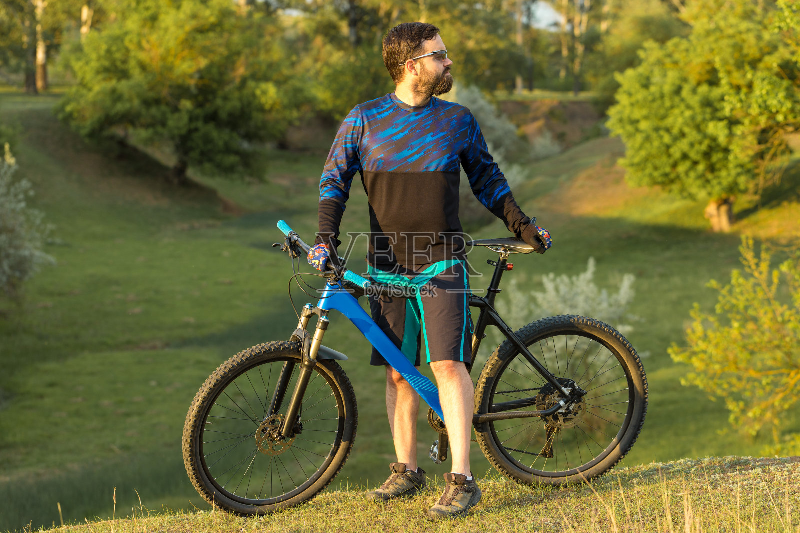 骑自行车的人穿着短裤和运动衫，骑着带有空气悬挂叉的现代碳硬尾自行车征服山峰。从山上看，美丽的景色。照片摄影图片