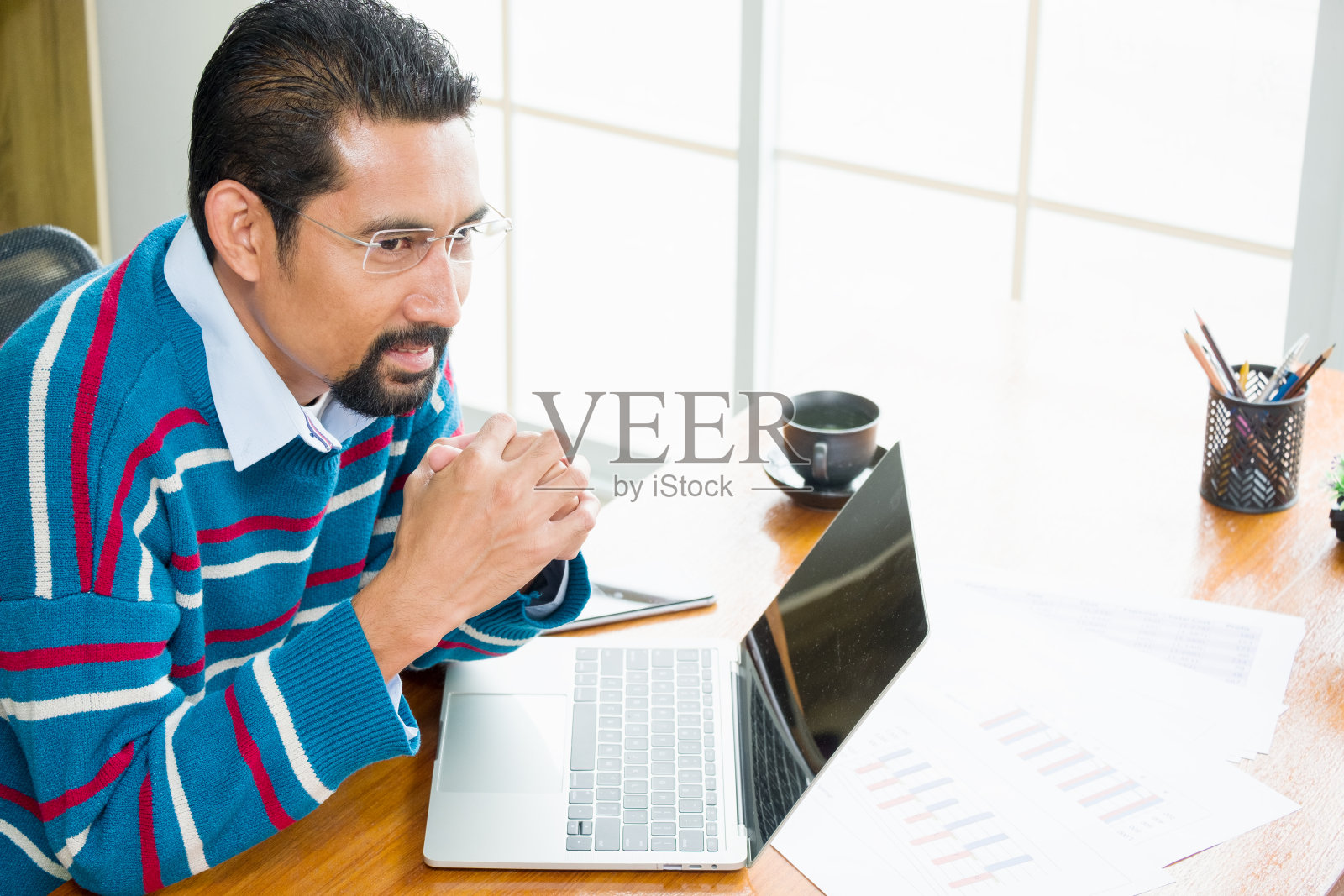 成年职业商人穿着长袖毛衣，在现代化的办公室里工作。长着胡须的英俊男子在自己家里的工作场所使用笔记本电脑。照片摄影图片