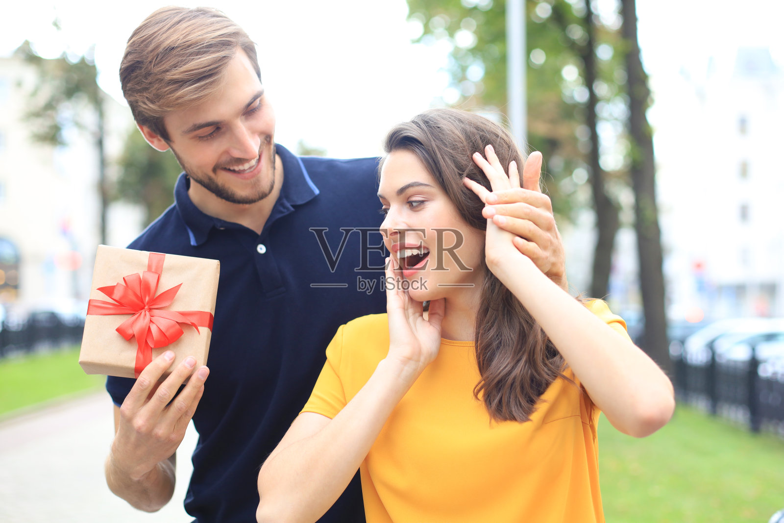 一对惊讶兴奋的情侣穿着夏装微笑着一起拿着礼物盒站在城市的街道上。照片摄影图片
