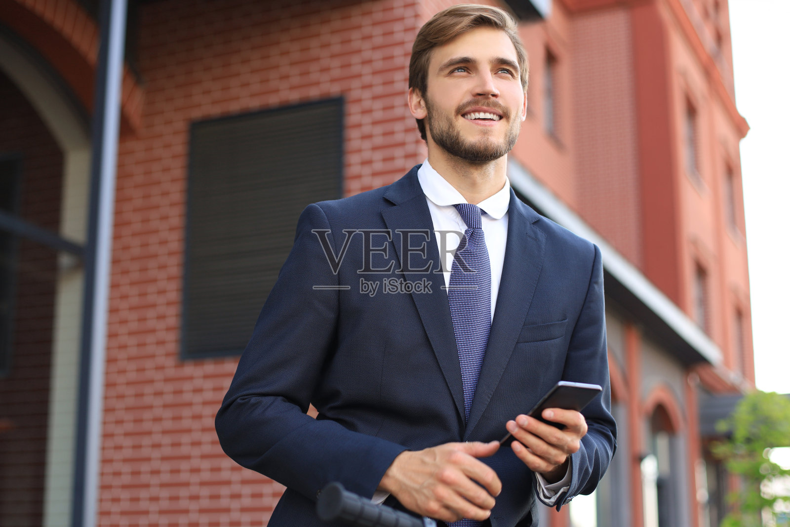 一个微笑的年轻商人穿着西装，站在户外用移动电话交谈。照片摄影图片