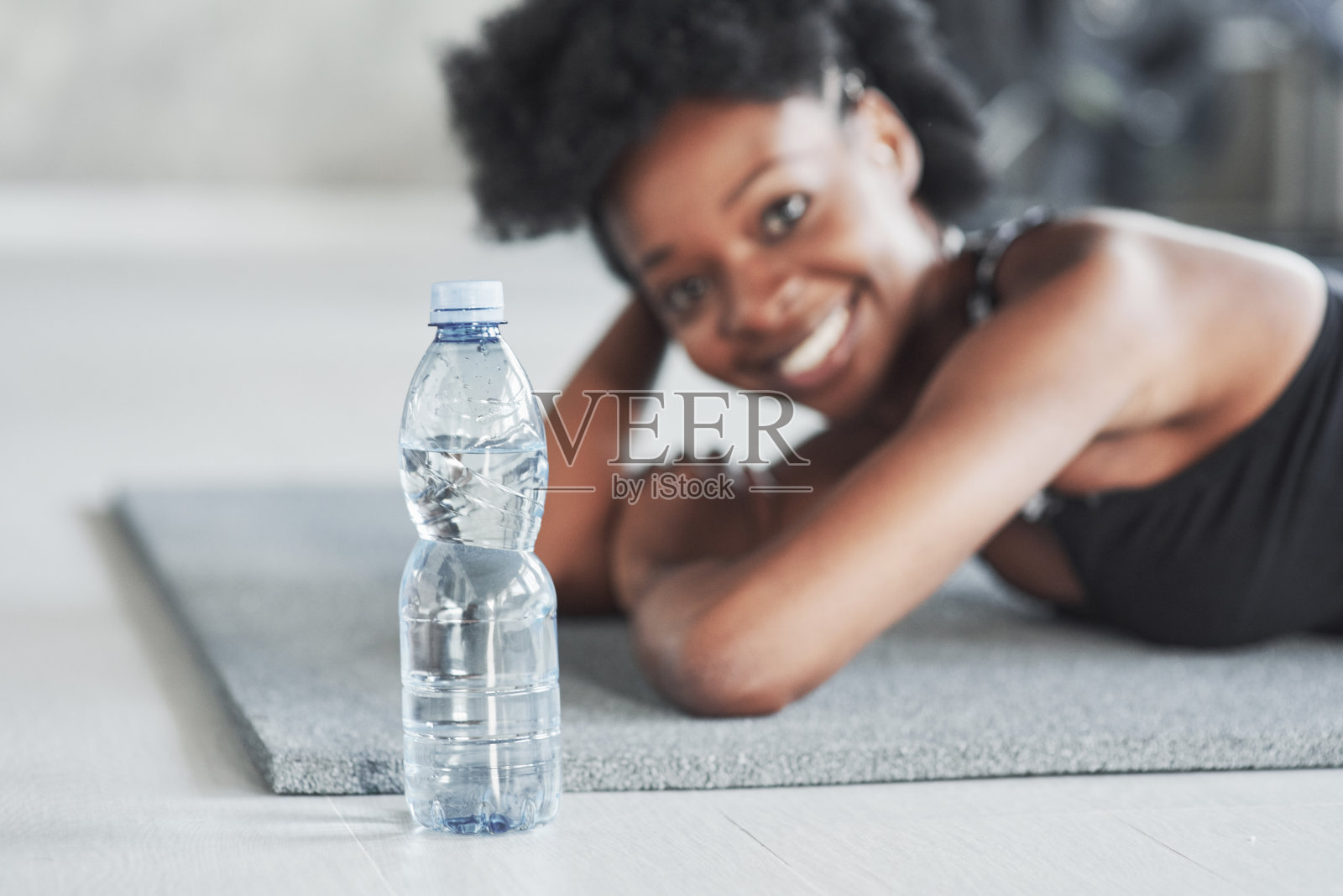 在女孩面前放一瓶水。非洲裔美国妇女卷头发和运动服有健身日在健身房照片摄影图片