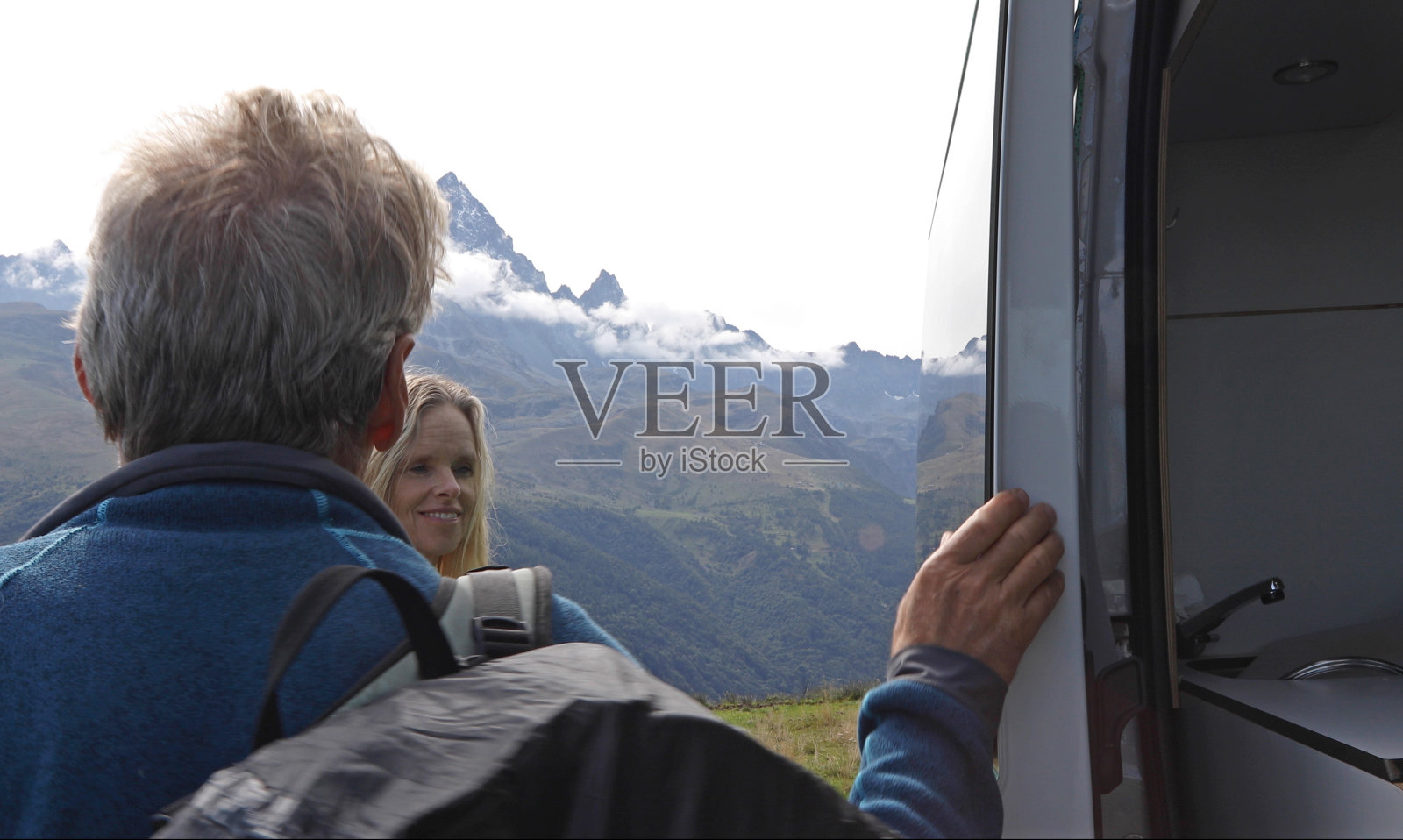 徒步旅行的夫妇在山中草地上倚靠着面包车的门放松照片摄影图片