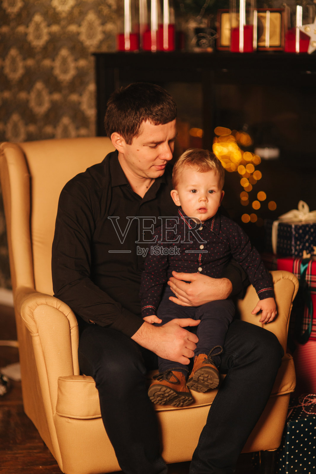 英俊的男人和儿子坐在家里的扶手椅上。圣诞节的气氛照片摄影图片