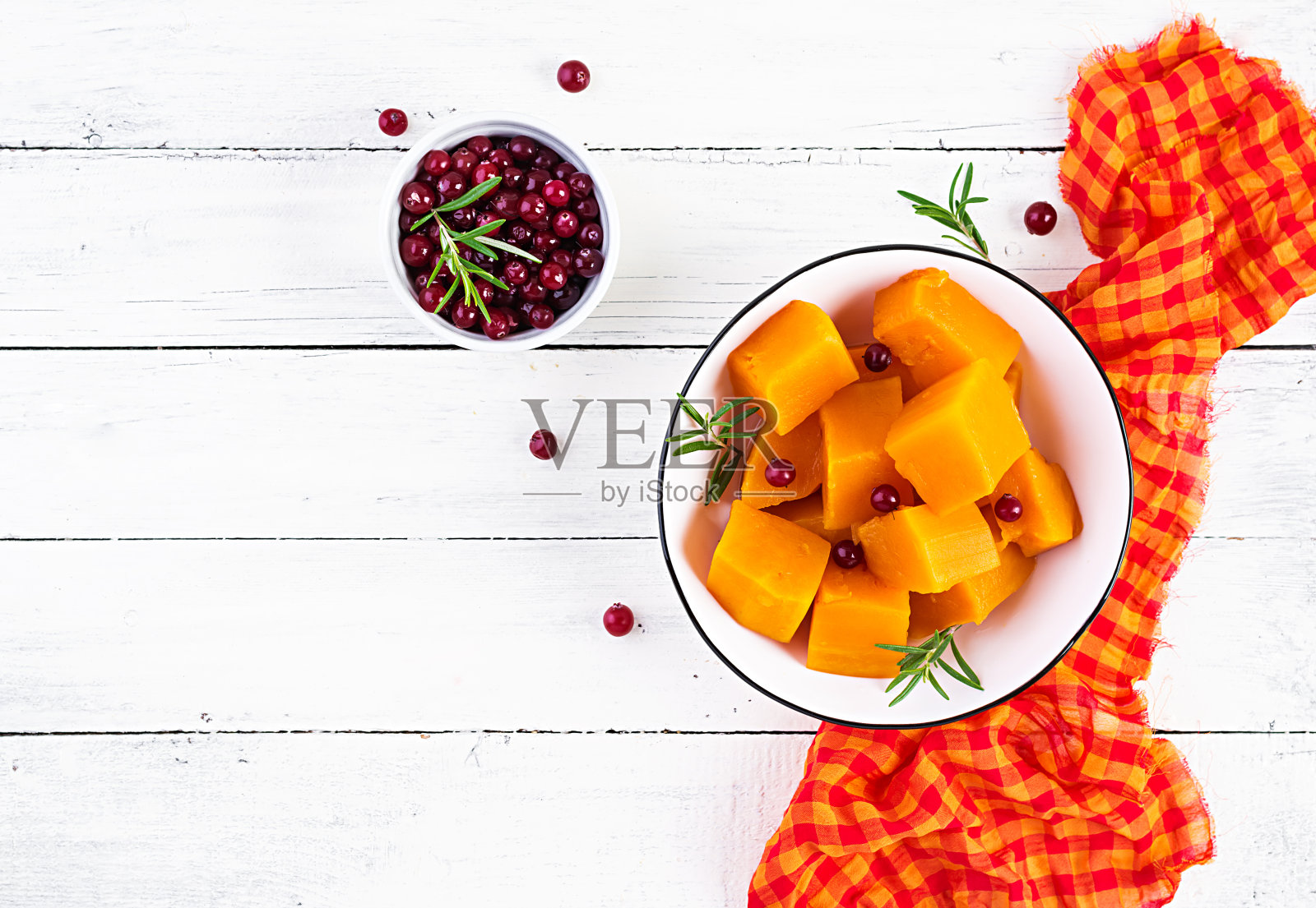 烤甜南瓜与迷迭香和蔓越莓在碗中，在白色的木制背景。从上面的观点照片摄影图片