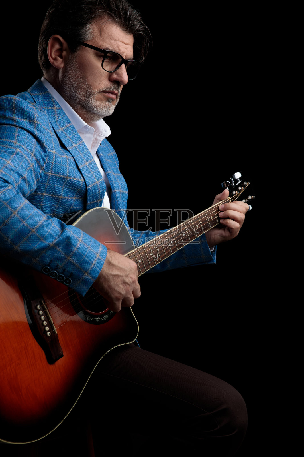 商人坐着，轻轻地弹着吉他，低头沉思照片摄影图片