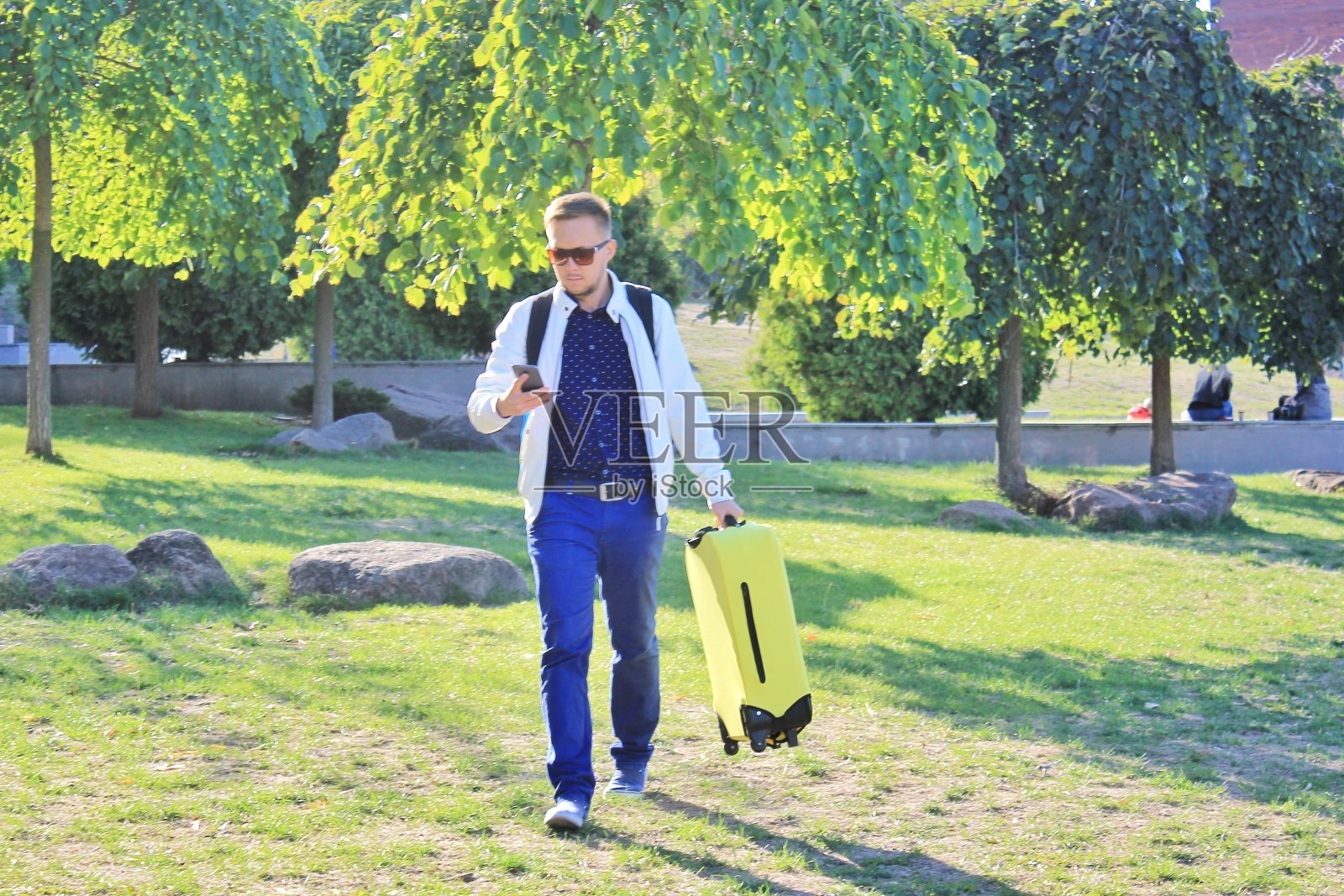 一名携带黄色行李的男子正在城市公园里等优步照片摄影图片