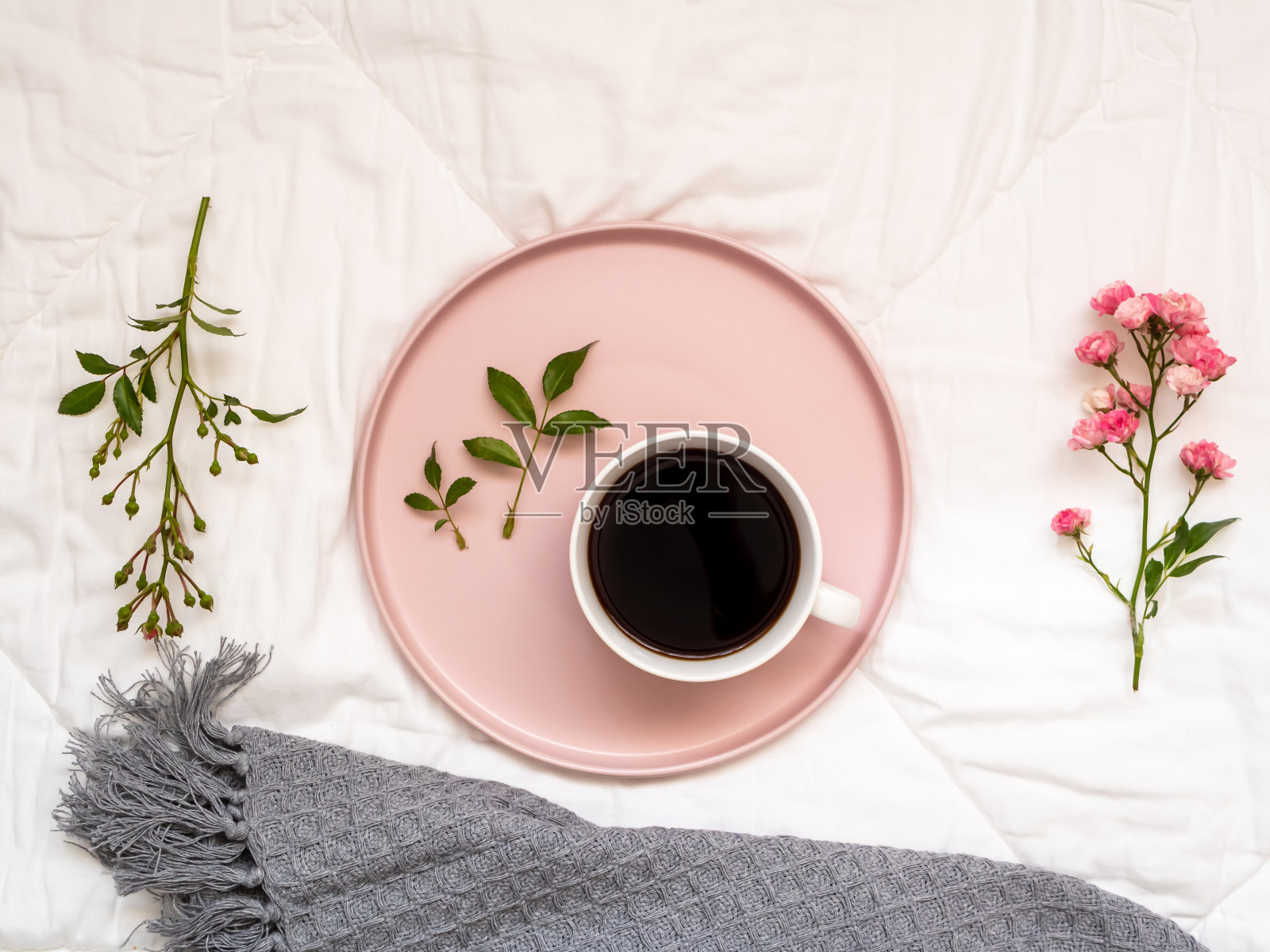粉色托盘上放着一杯咖啡，白色被单上放着花朵照片摄影图片
