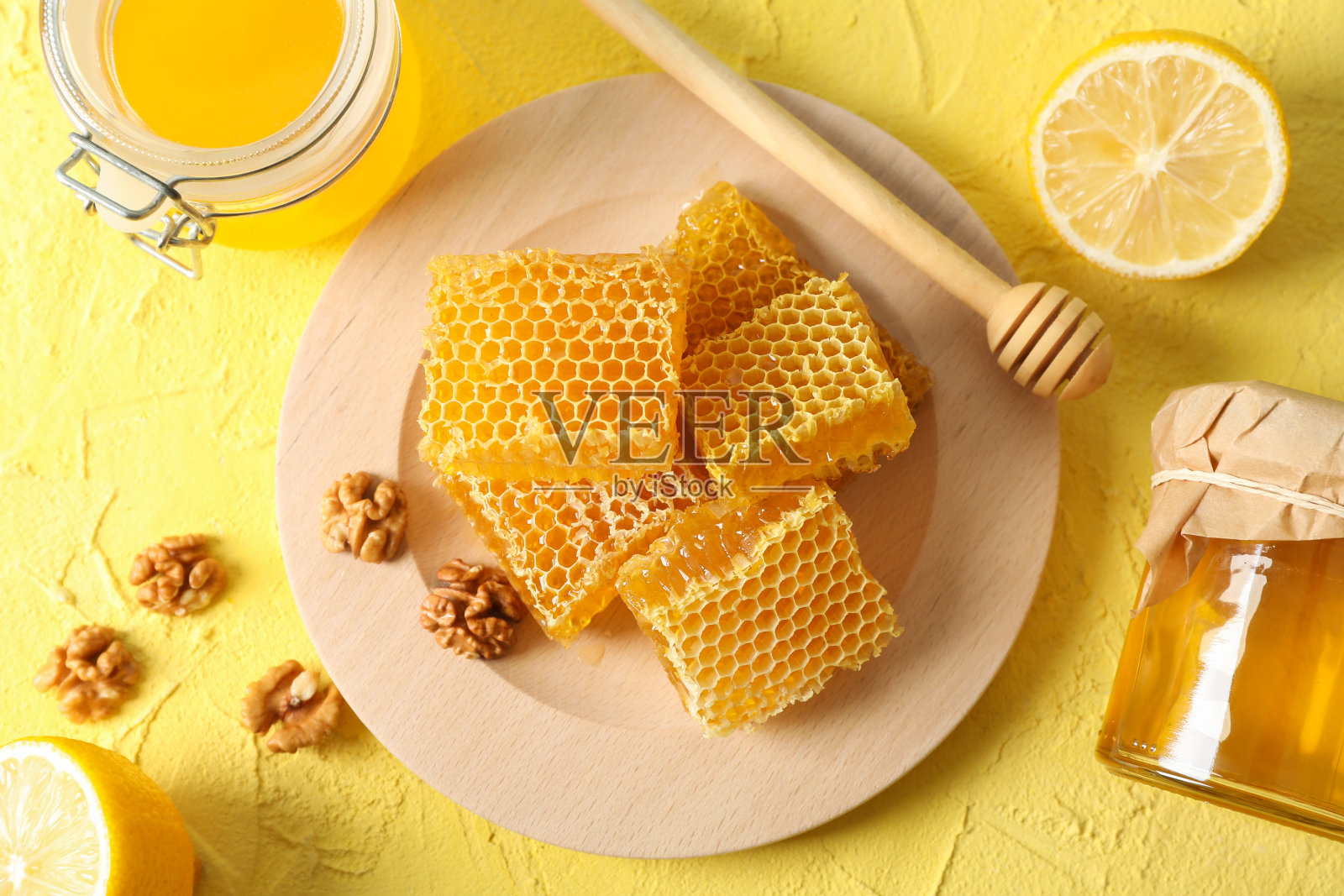 胡桃木，蜂巢，蜂蜜罐，勺子和柠檬黄色背景，俯视图照片摄影图片