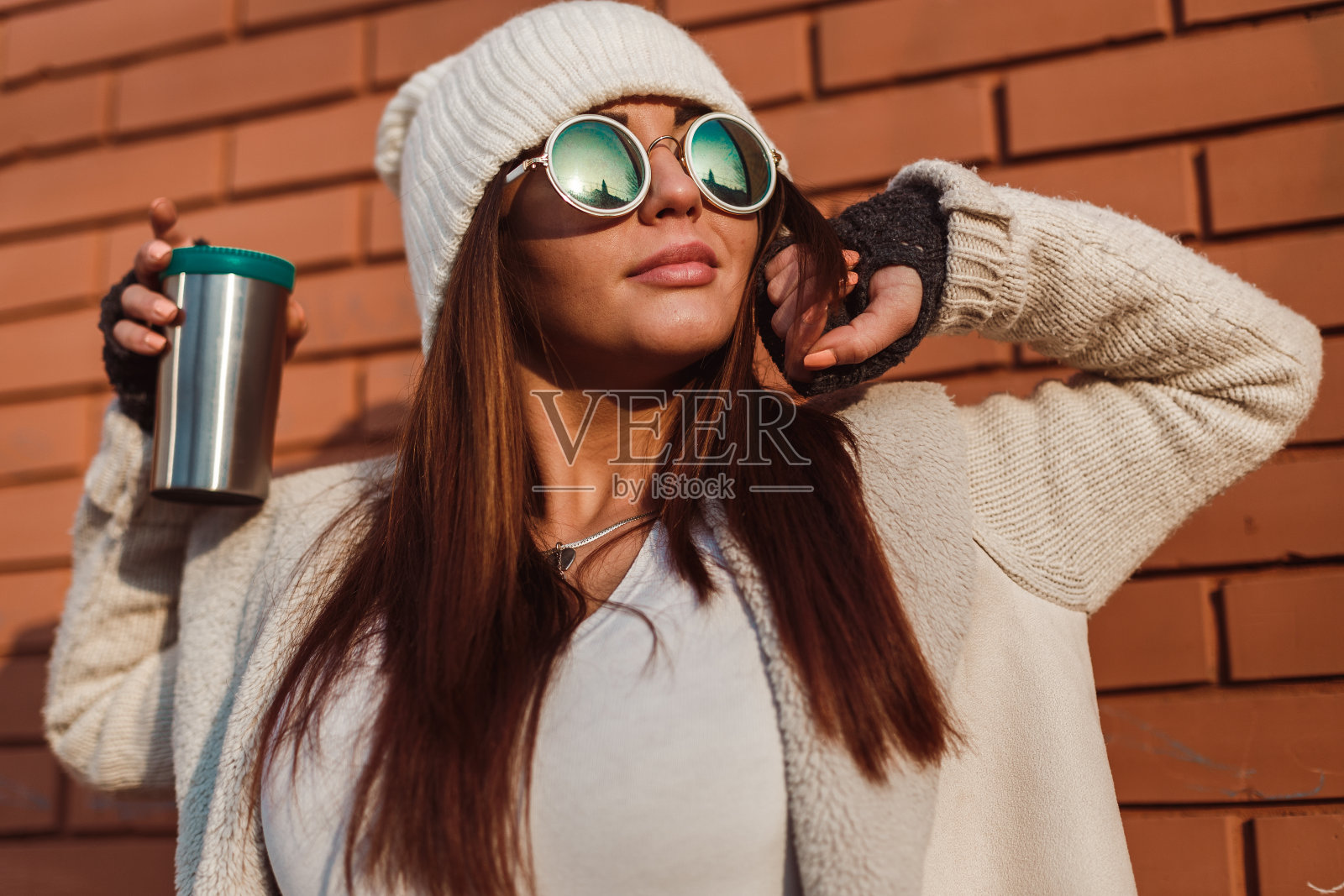 女人戴着针织帽，拿着可重复使用的咖啡杯在户外照片摄影图片