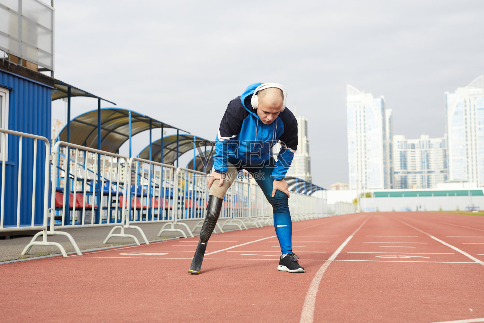 精疲力竭的光头青年残疾人跑步刀累后，靠在膝盖上深呼吸照片摄影图片