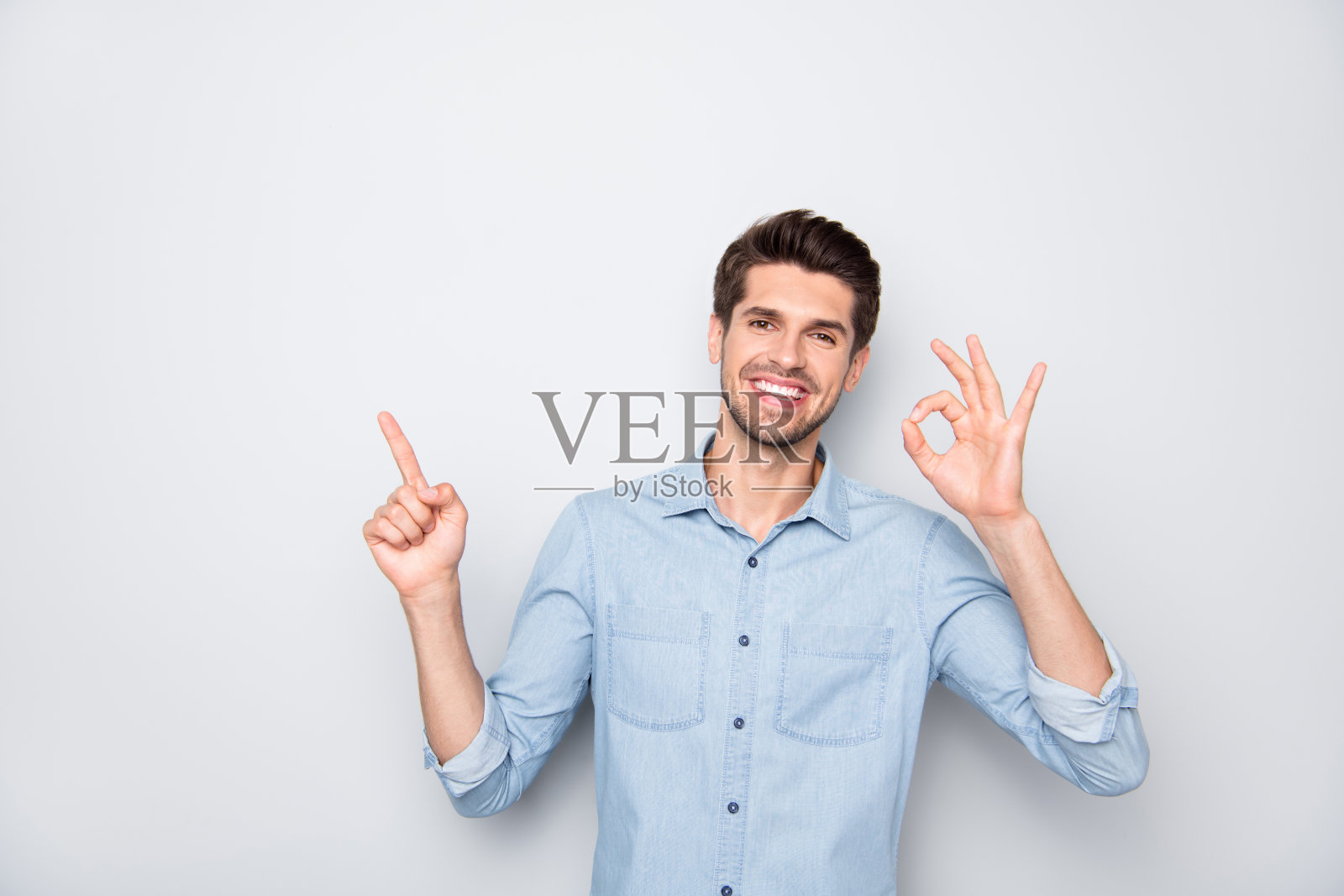 积极开朗的家伙的肖像发起人点食指显示ok标志建议广告广告促销穿牛仔牛仔裤装孤立的灰色背景照片摄影图片