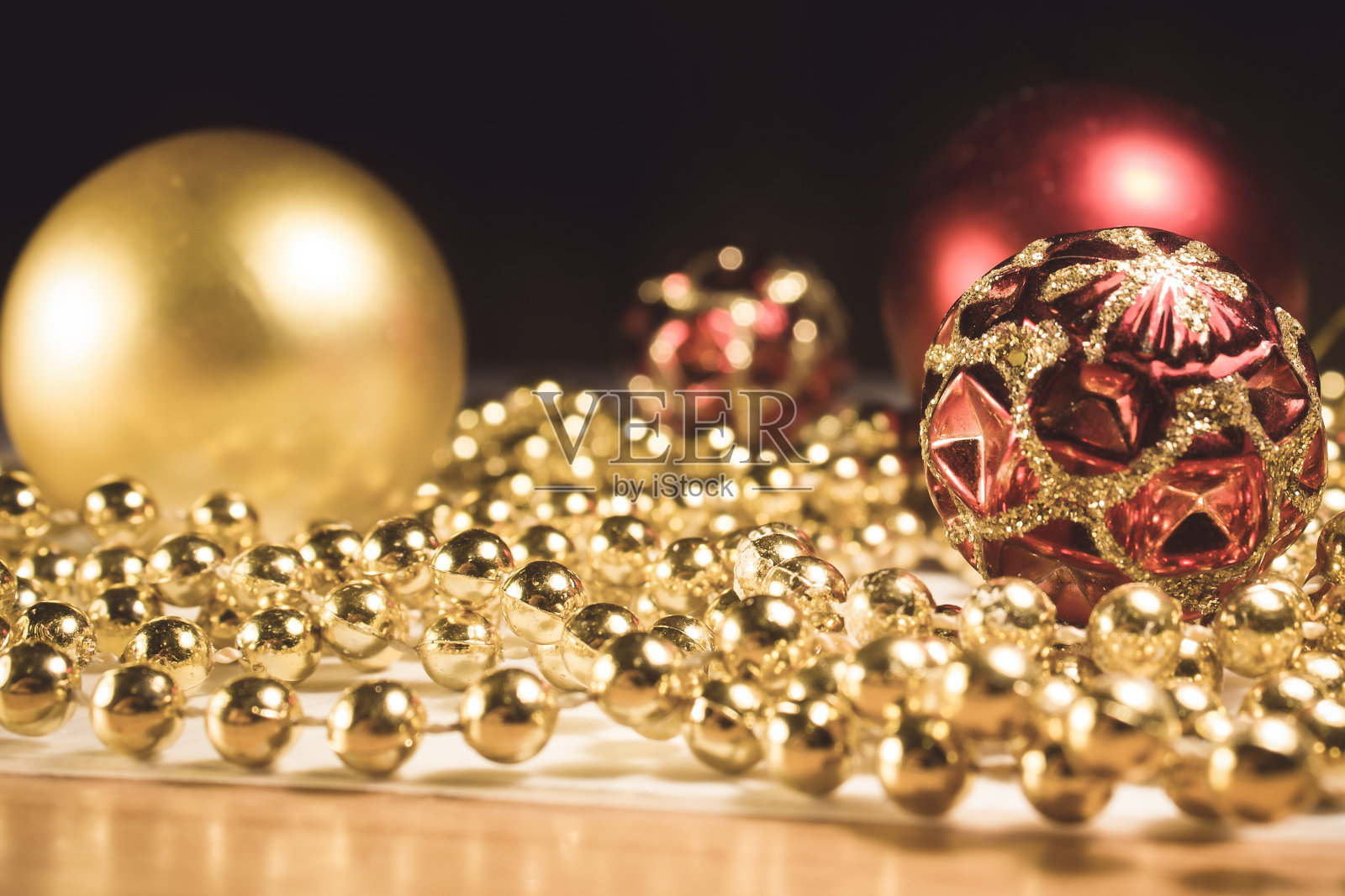 圣诞玩具与珠子在桌子上一个黑色的背景。红色和金色的珠子。有闪亮图案的圣诞玩具。照片摄影图片