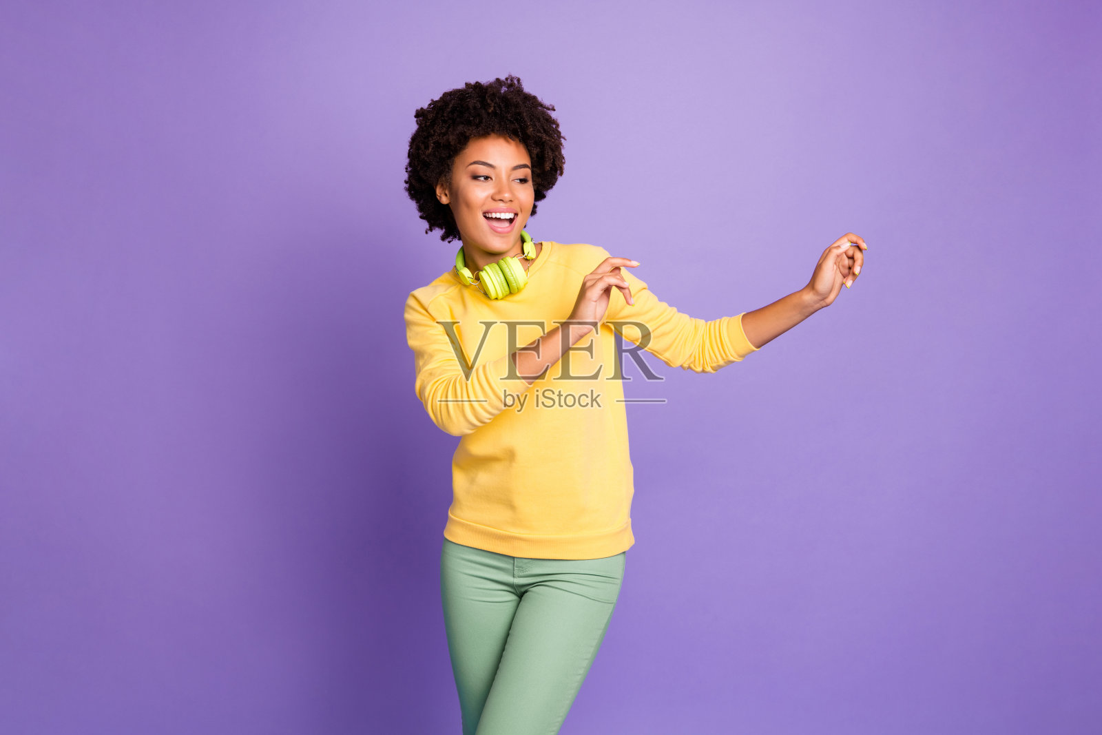 卷曲波浪的照片，欢快的积极的funky舞者穿着绿色裤子裤子与耳机在孤立的紫色柔和的颜色背景照片摄影图片