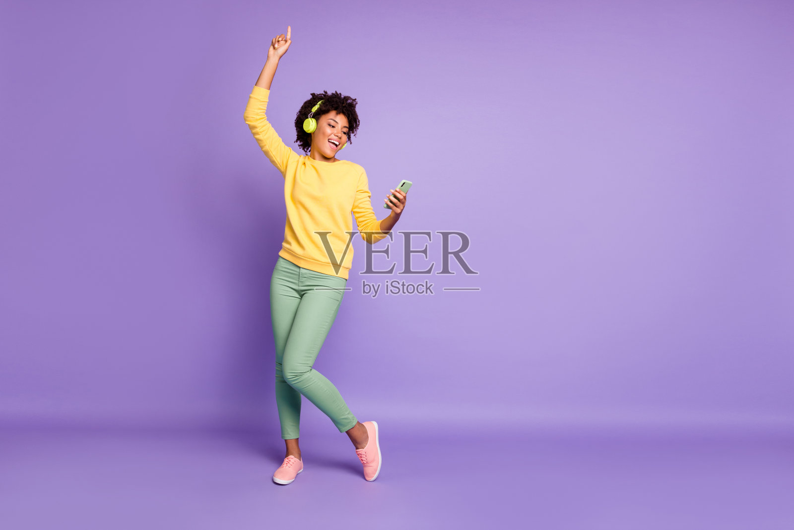 丰满的身体尺寸的照片，卷曲的波浪时尚甜美可爱迷人的无忧无虑的女孩跳舞和唱歌，而阅读她的电话上的歌曲文本和戴耳机孤立的紫色柔和的颜色背景照片摄影图片