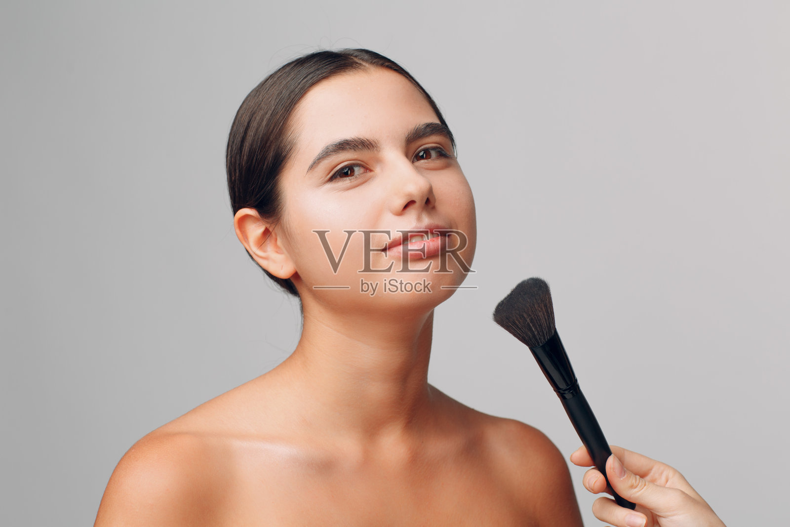 化妆师应用化妆。美丽的女人的脸。化妆师手，年轻的美容模特女孩。在过程中弥补。照片摄影图片