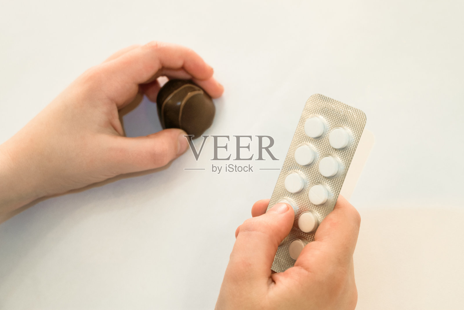 甜食和糖的危害。孩子一手拿着一包药丸和巧克力糖。有选择的集中在一只手上的药丸。照片摄影图片