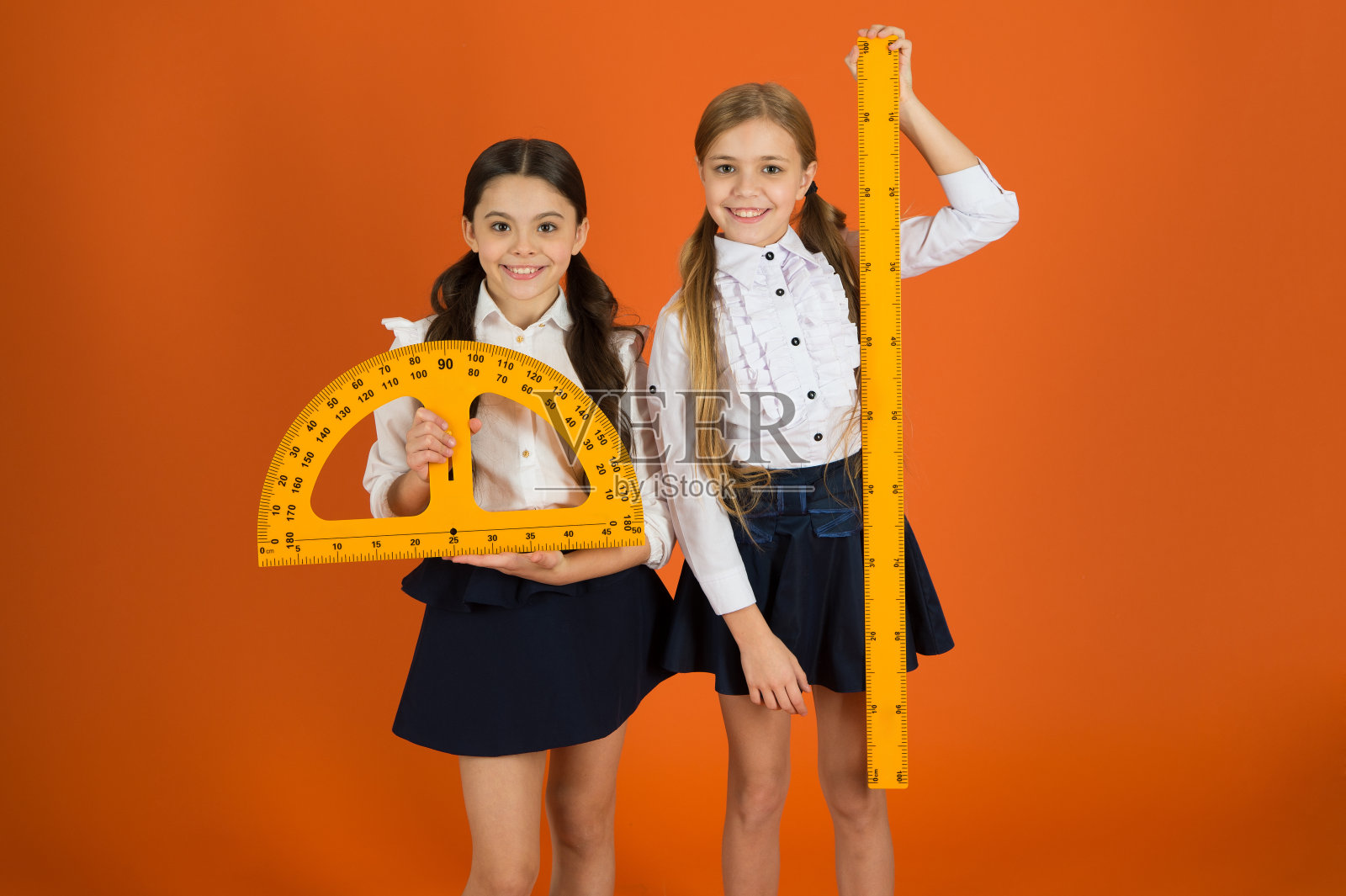 小学生可爱的女孩与大尺子。几何最喜欢的科目。教育和办学理念。学校学生学习几何。橙色背景的孩子校服。阻止学校学科照片摄影图片