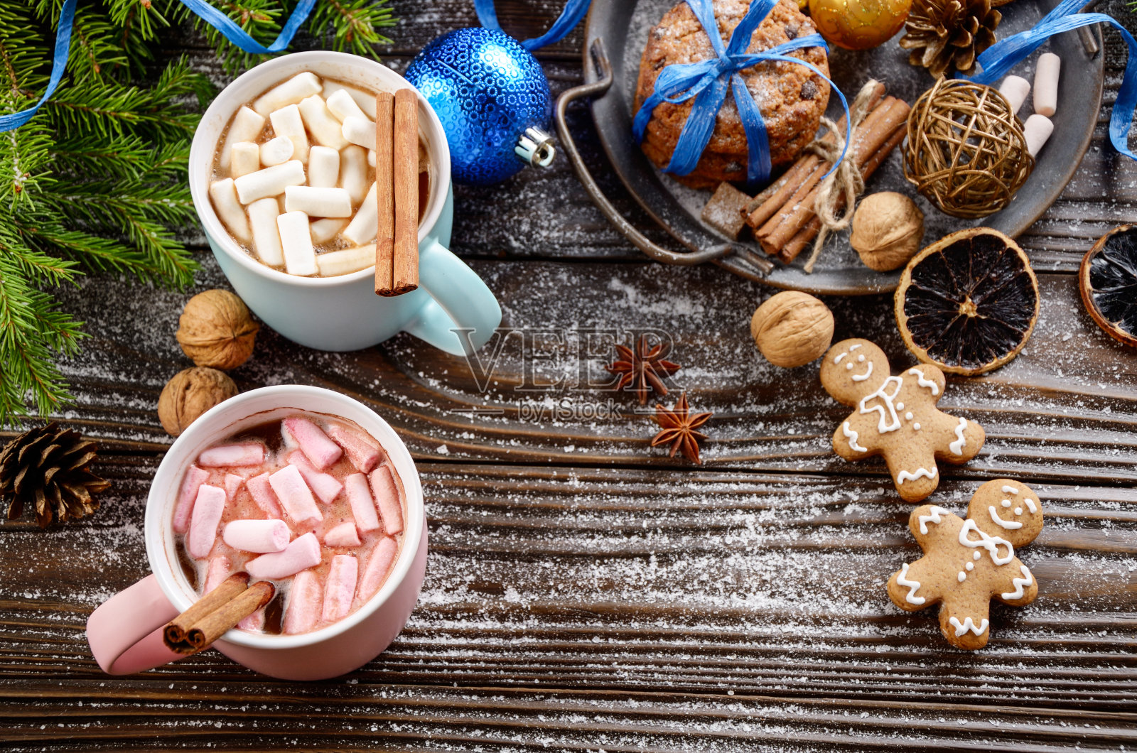 木桌上平铺着圣诞节的背景:两杯热巧克力配棉花糖、云杉枝和托盘，托盘上还有姜饼人饼干照片摄影图片