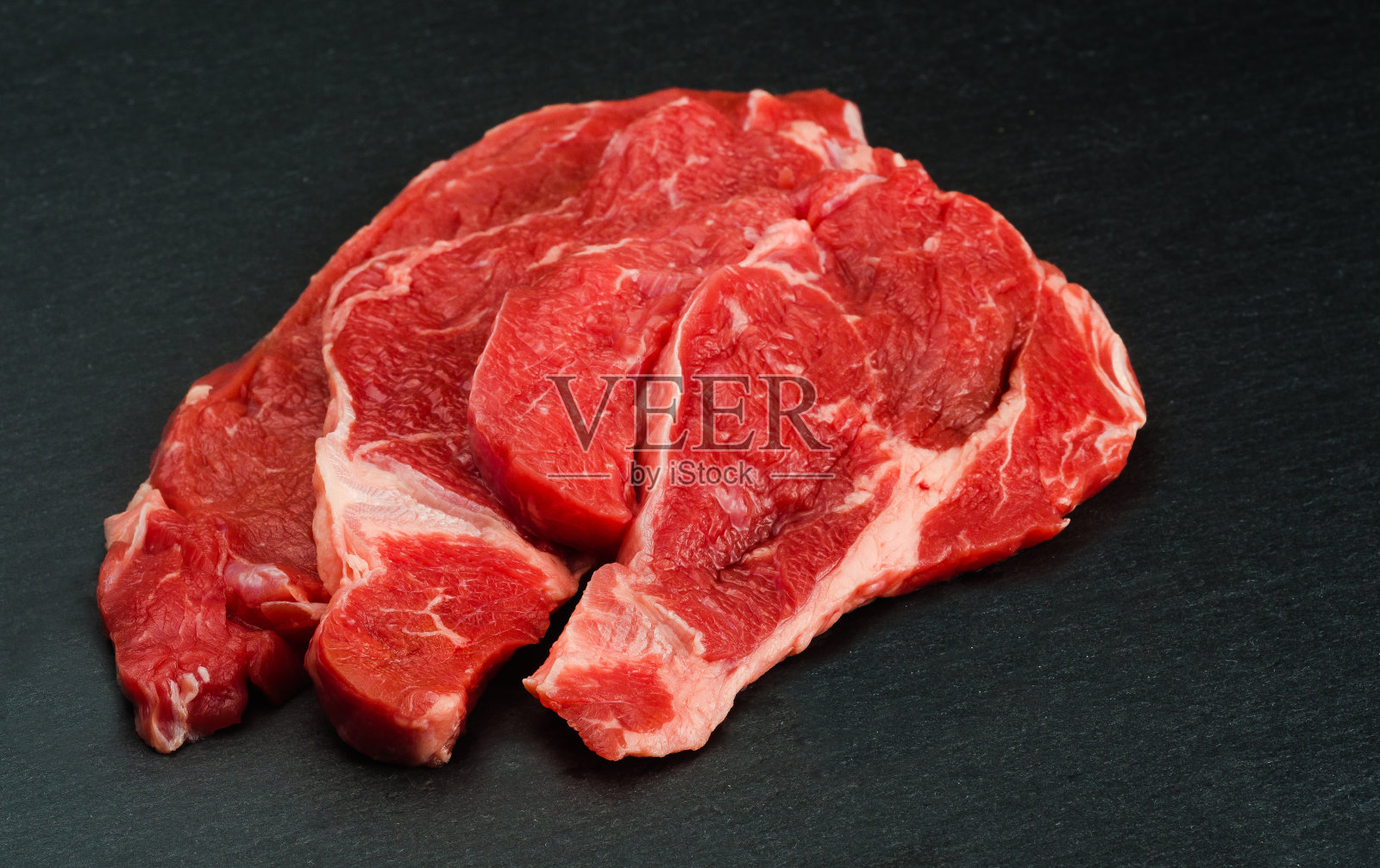 新鲜的生肉。准备烹调的生牛肉。背景黑色的黑板上照片摄影图片