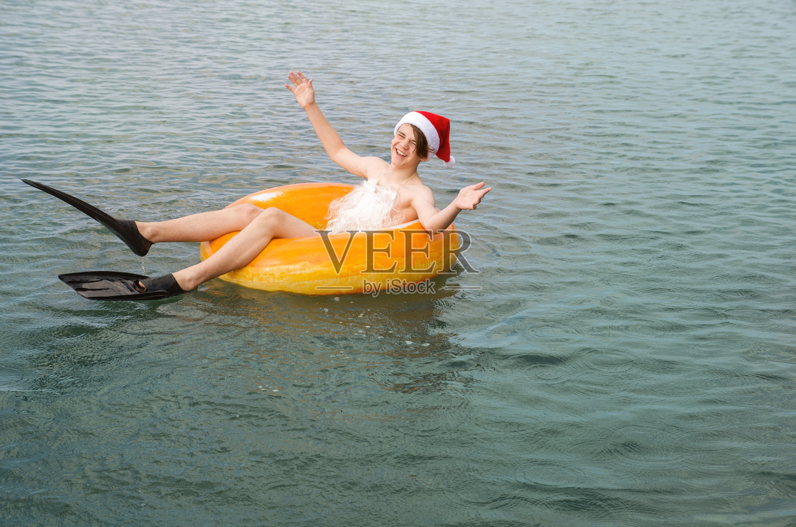 十几岁的男孩穿着脚蹼，戴着圣诞帽，骑着充气圈在海浪上游泳和休息照片摄影图片