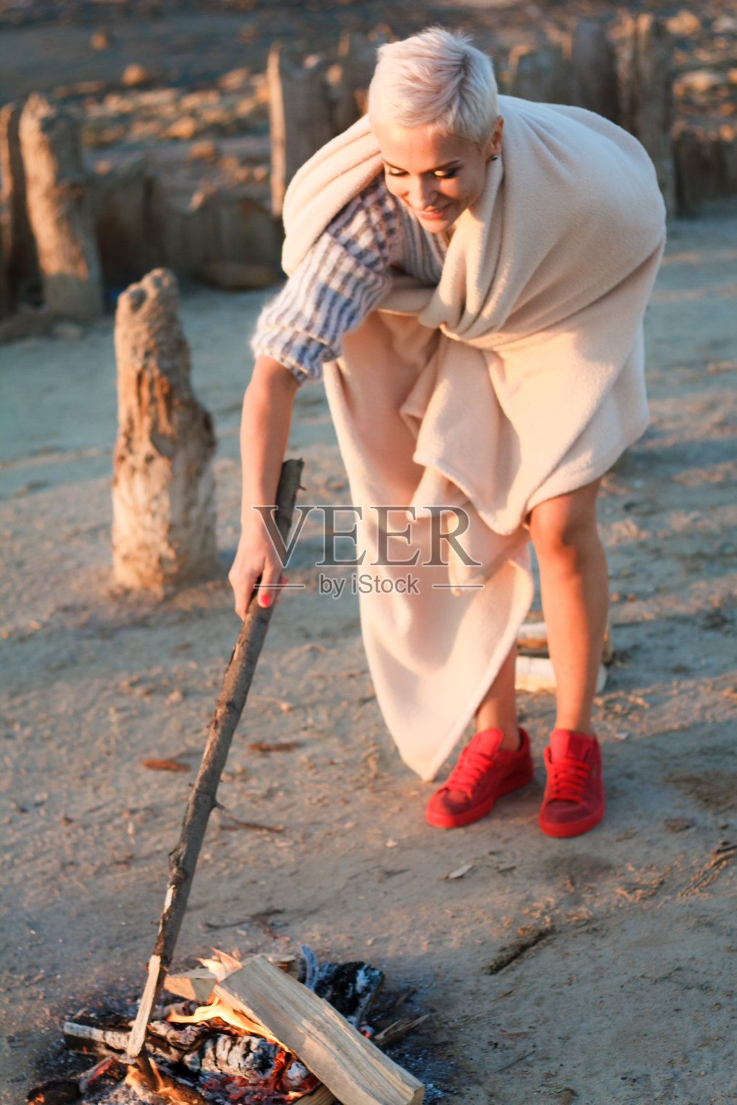 成年中年金发女人在一件毛衣坐在火上的日落海滩上，选择性的焦点照片摄影图片