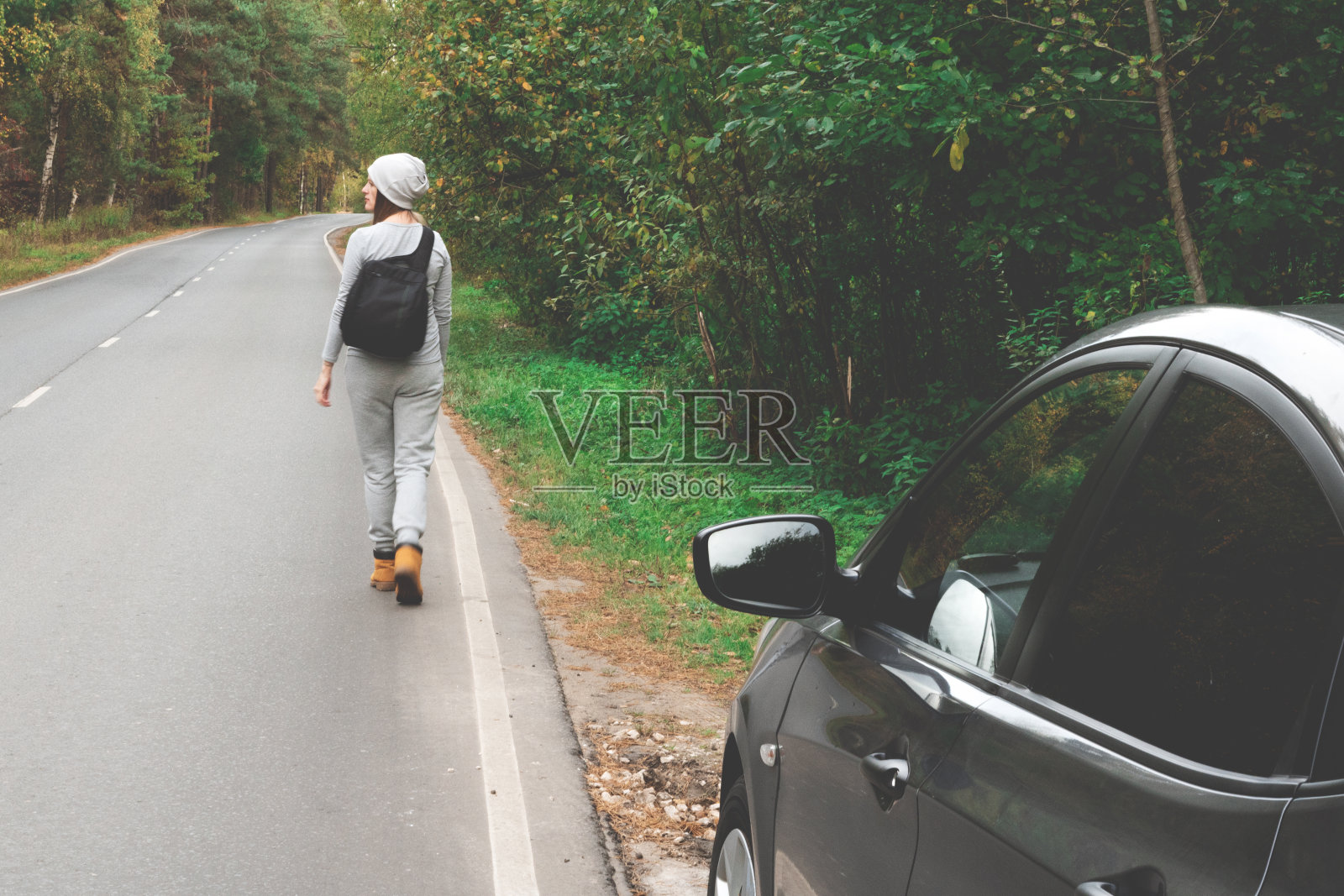 一个背着背包的年轻女子正走在空旷的秋路上。旅行,潮人。走在秋天，秋天的树照片摄影图片