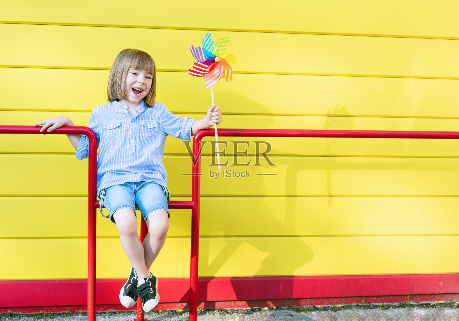 孩子拿着风车玩具站在黄色的墙前照片摄影图片