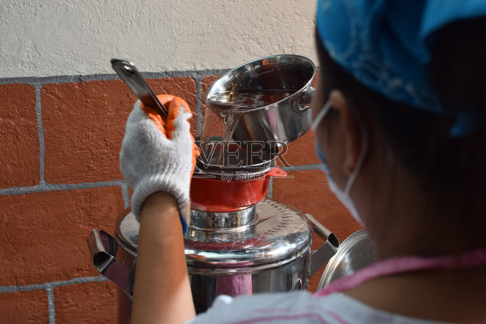 在一个以家庭为基础的酿酒厂，妇女在不锈钢分配器中倒入发酵的酒精果汁。后拍摄照片摄影图片