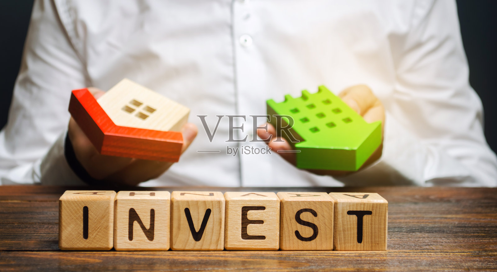 写着“投资”的木块和商人手中的房子。投资房地产建设的概念。有效的投资。购买公寓。商业和金融照片摄影图片