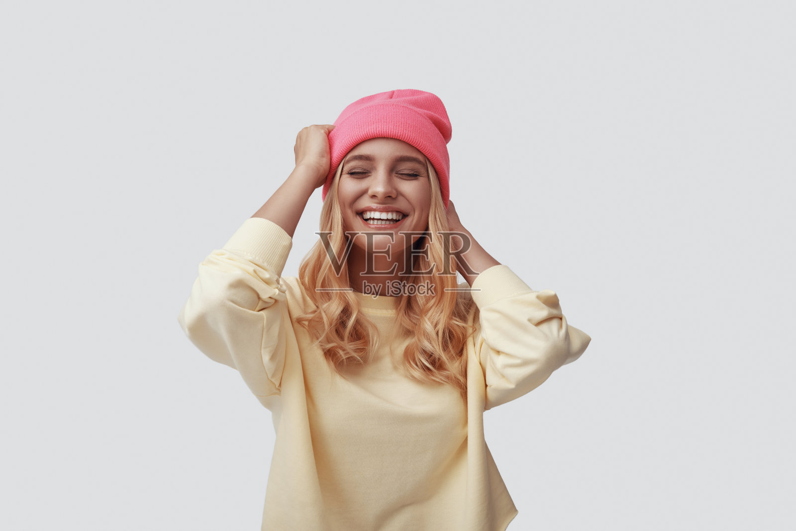 迷人的年轻女子在粉红色的帽子微笑，而站在灰色的背景照片摄影图片