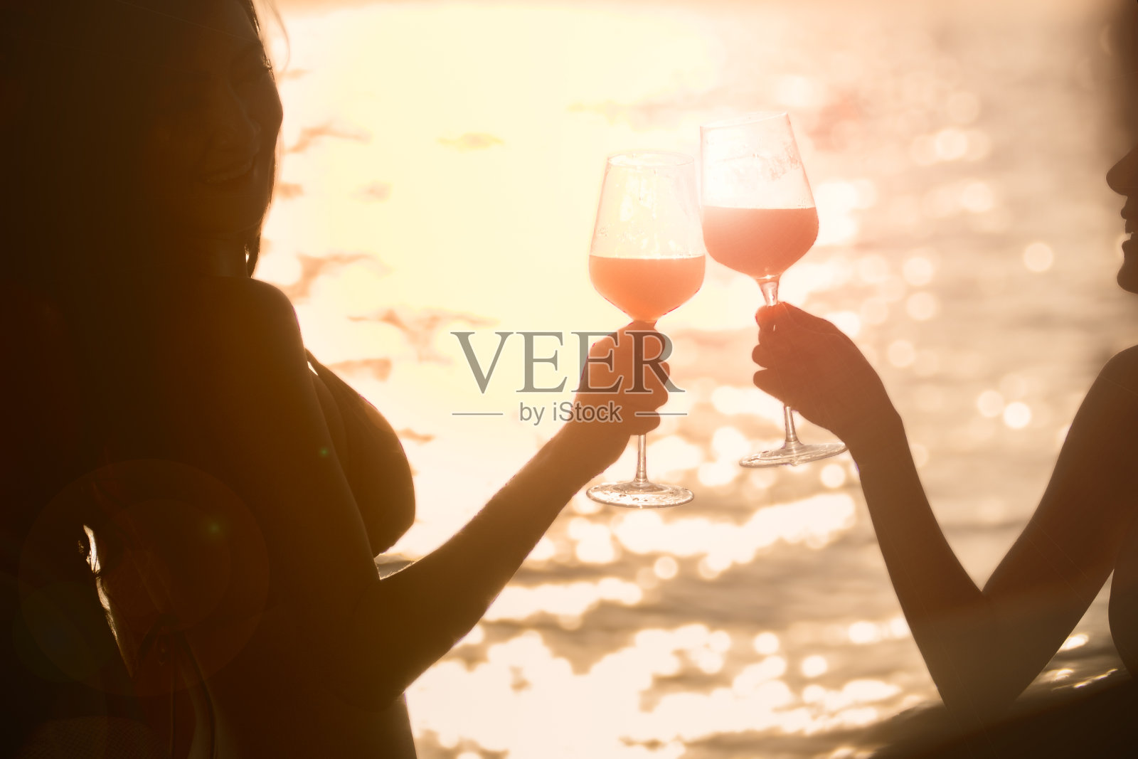 美丽的女人举杯与她的葡萄酒在周年聚会与海背景镜头耀斑阳光。照片摄影图片