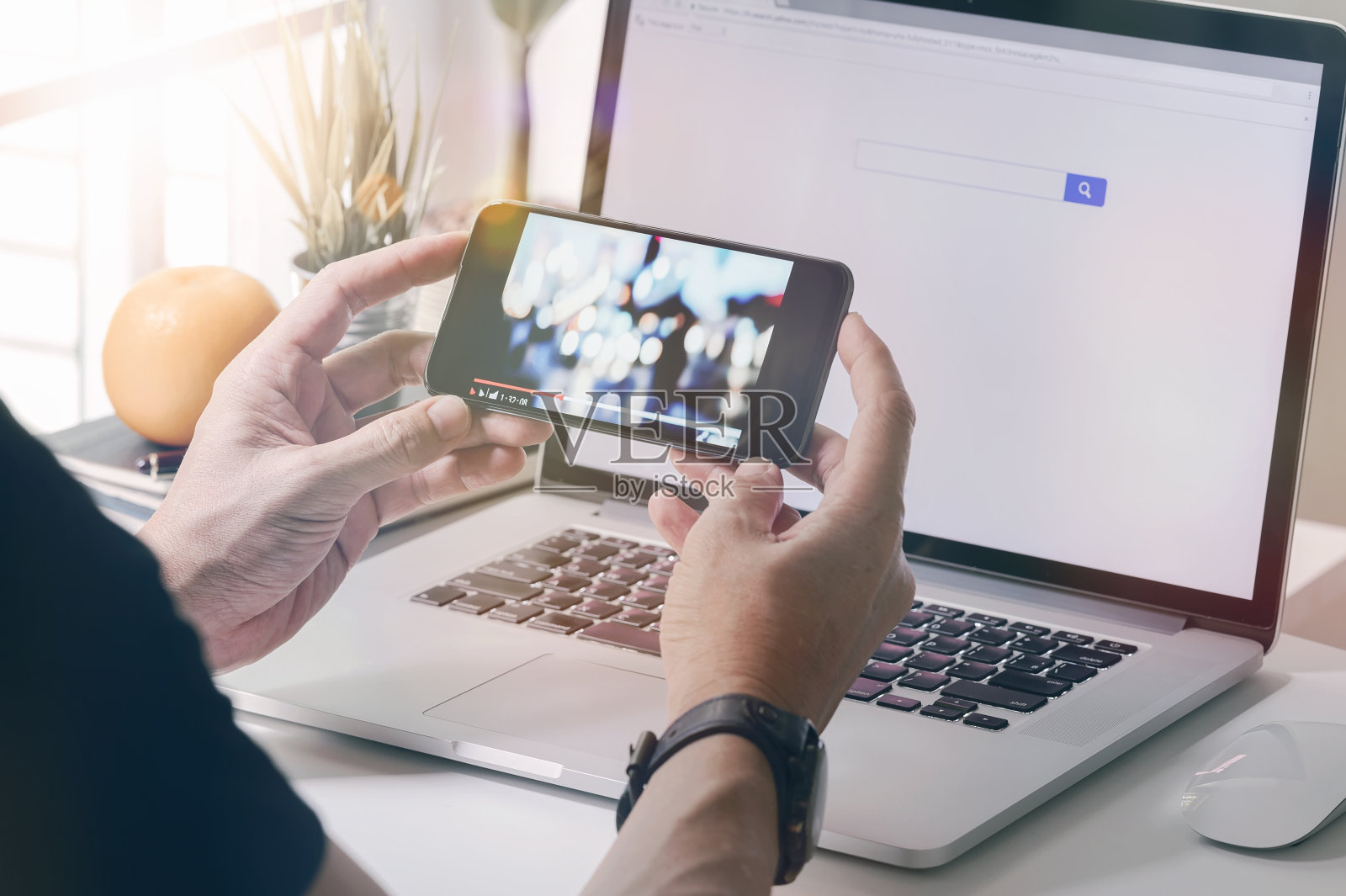 男人用智能手机看视频，而坐在办公桌上用笔记本电脑。照片摄影图片