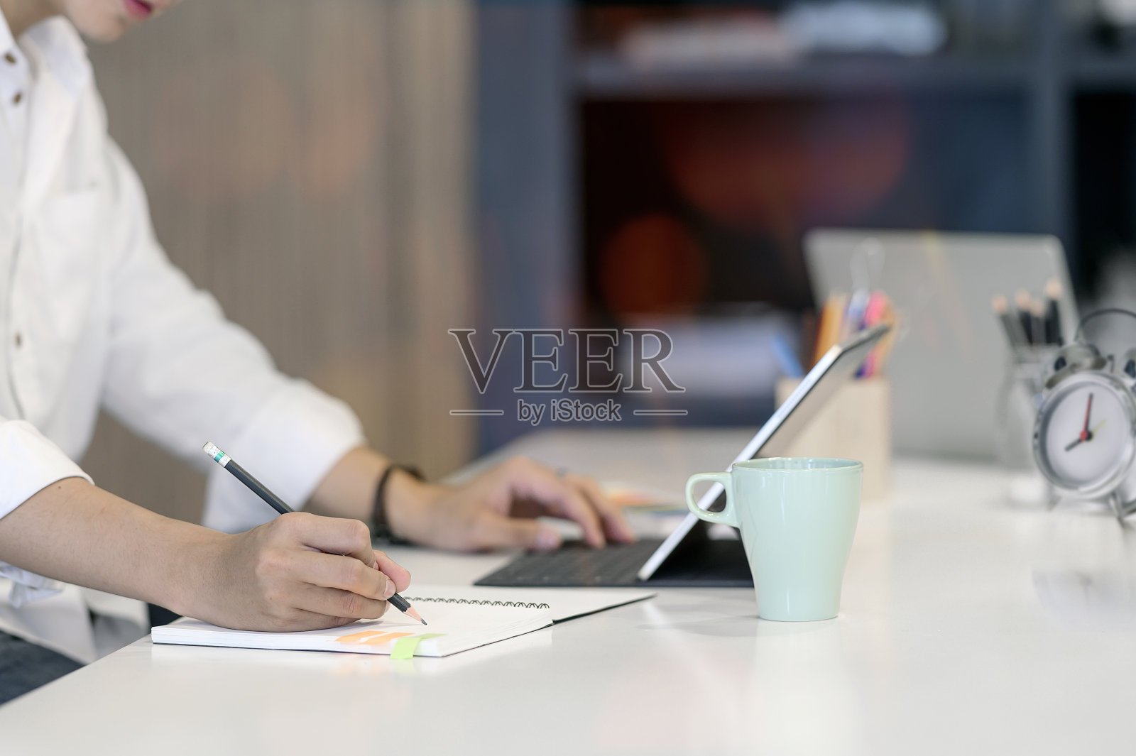 一名男子坐在办公桌前用铅笔在笔记本上写字。照片摄影图片