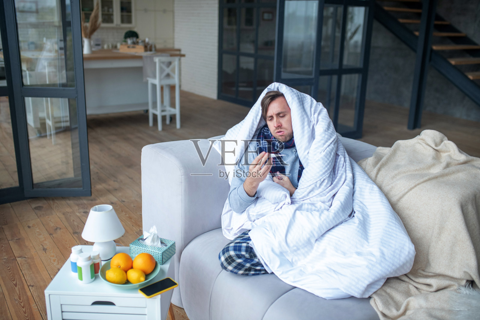 病人盖着床罩坐在沙发上，感觉糟透了照片摄影图片