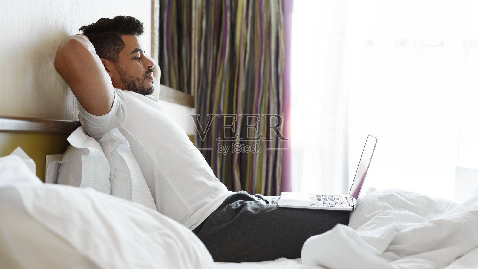 在床上听音乐、使用笔记本电脑的放松帅哥照片摄影图片