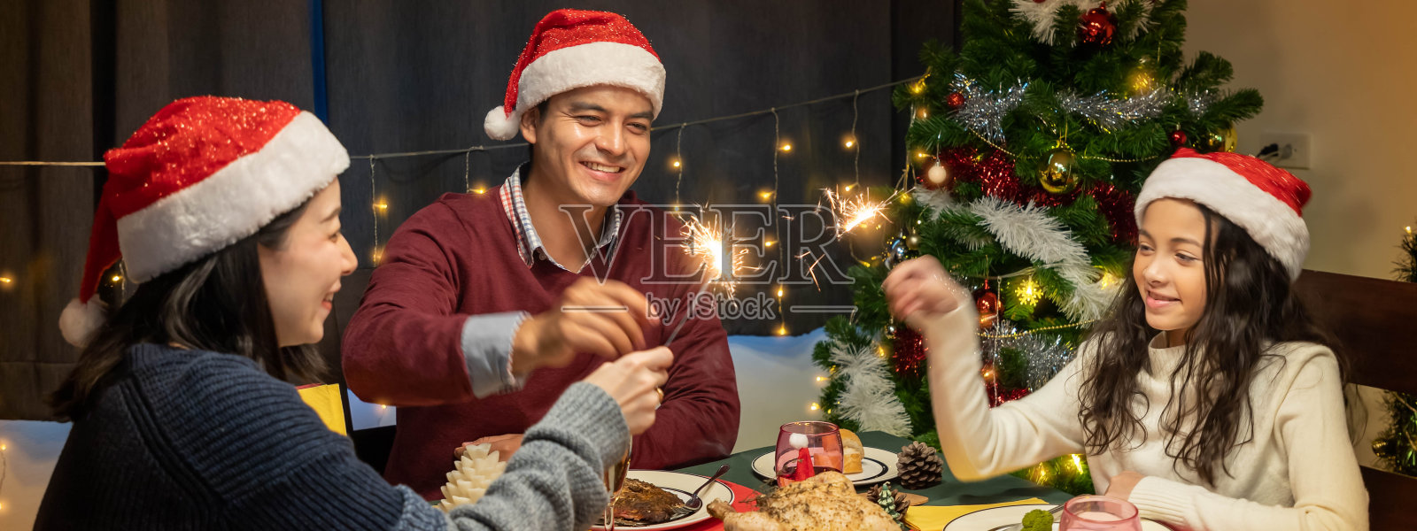 幸福的一家人，爸爸妈妈和女儿，一起吃晚饭，一起庆祝圣诞节的节日，用闪闪发光照片摄影图片