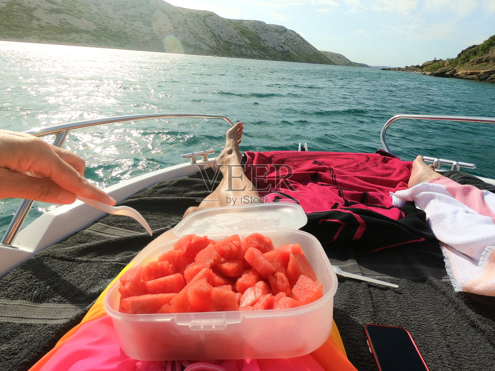 男人和女人的腿躺在游艇上，以碧蓝的大海和海滩为背景，吃着西瓜。奢华的夏日度假概念。照片摄影图片