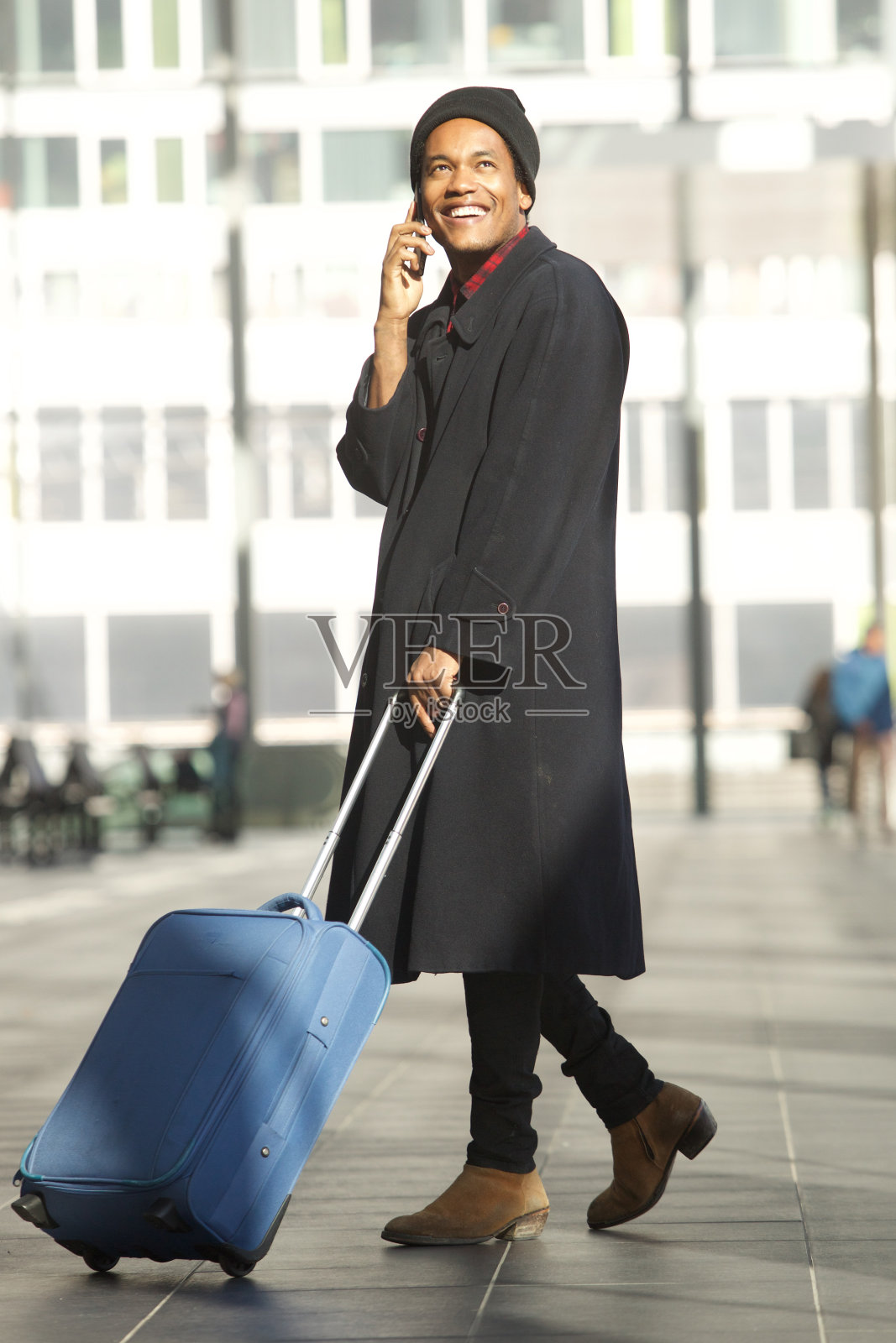 全身微笑的非洲裔美国旅行男子走在车站，带着手机和行李箱照片摄影图片
