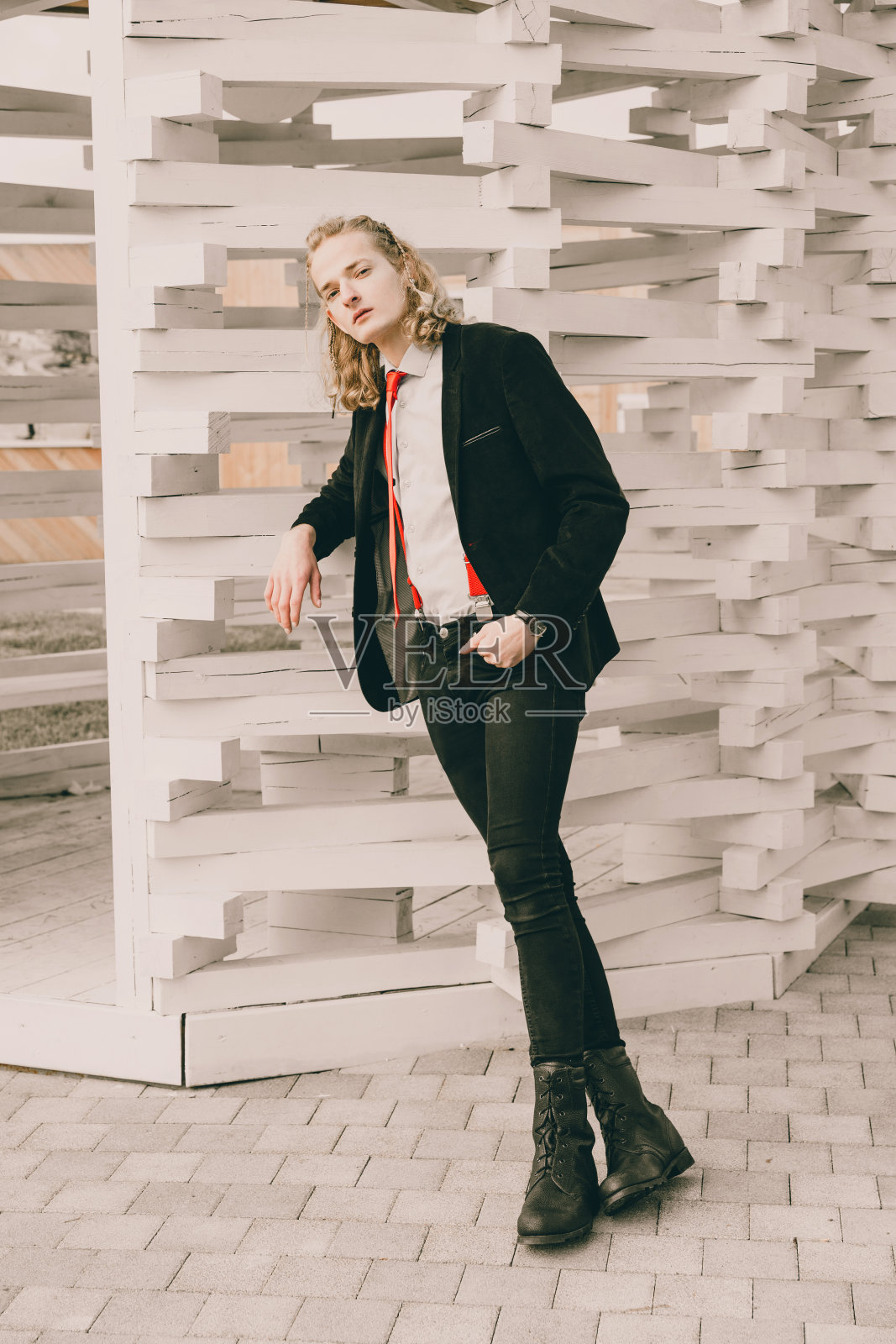 一幅年轻男子的肖像，身穿黑色西装，打着红色领带，倚在一个白色木凉棚上。照片摄影图片