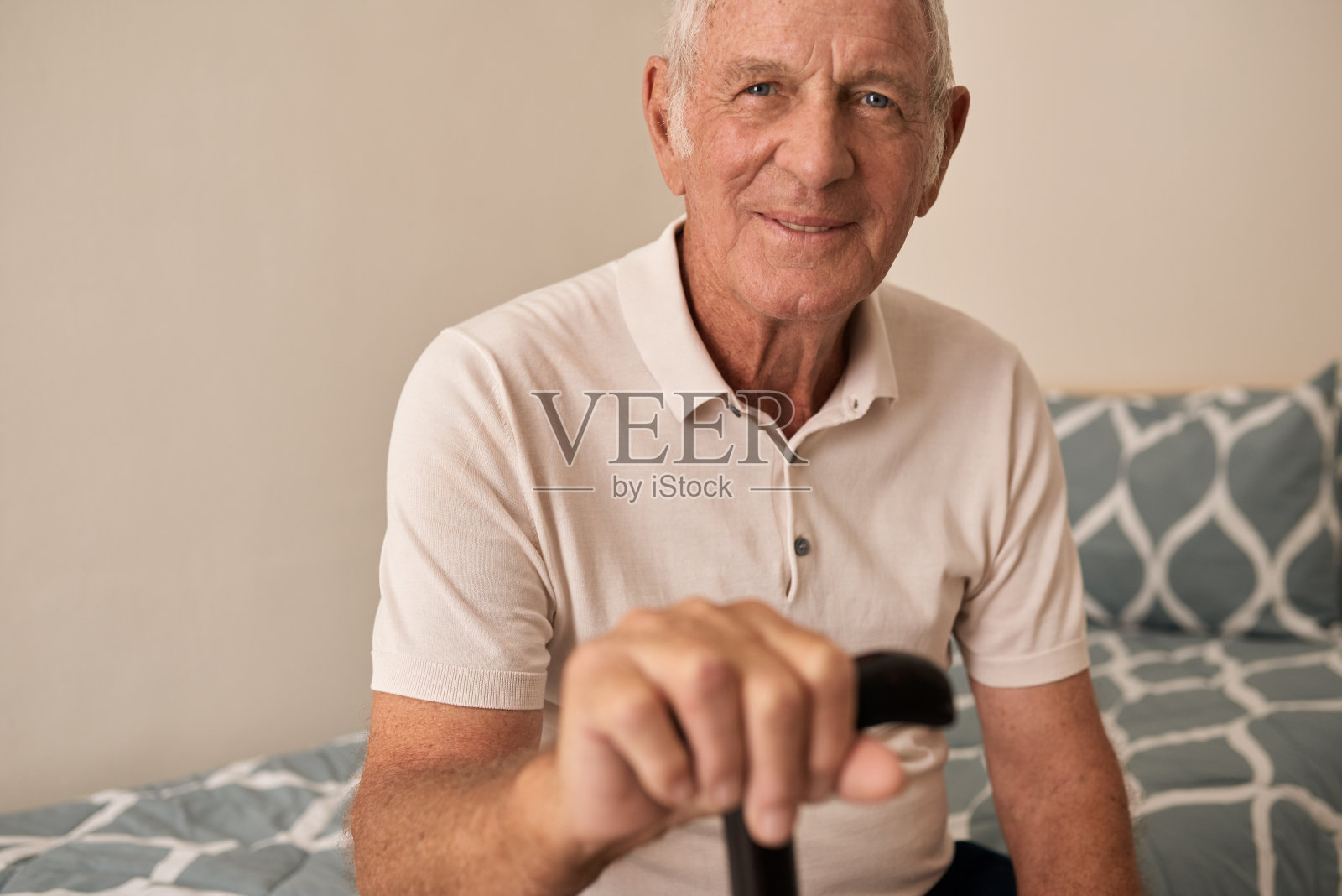 微笑的老人坐在他的床上，拿着他的手杖照片摄影图片