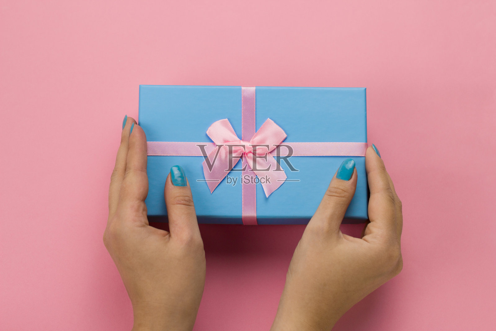 女性手握蓝色礼盒与节日粉红色蝴蝶结在一个柔软的粉红色背景照片摄影图片